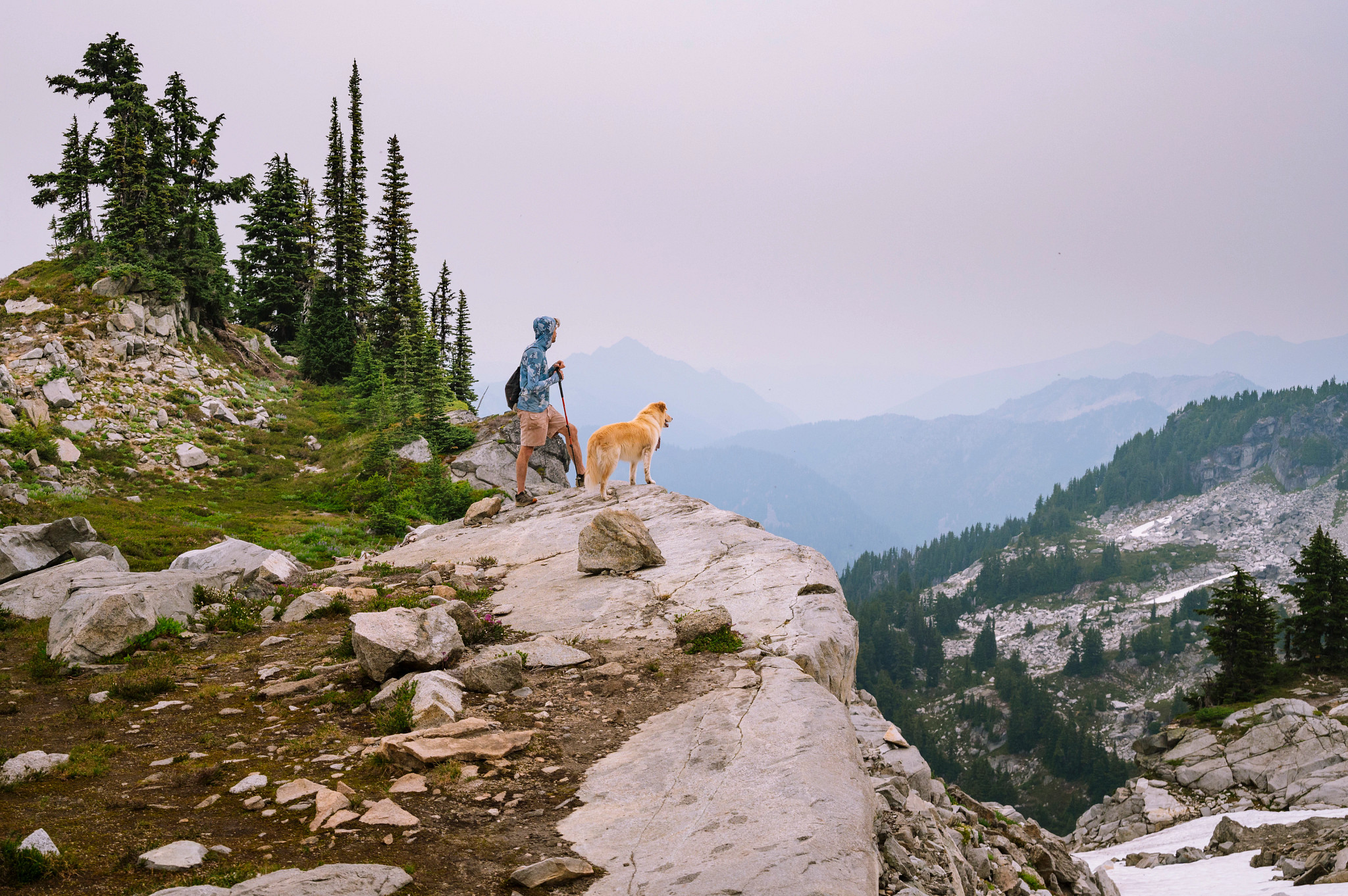 a man and a dog standing on a cliff while looking at mountains