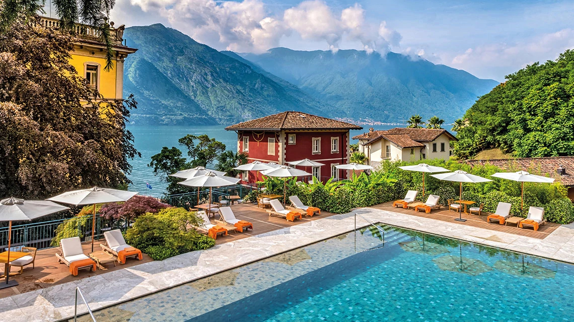 villa pool with chairs and umbrellas sunny day, river in background with mountains