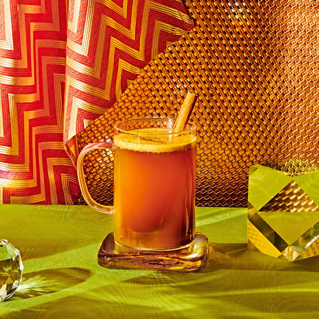 Warm spiced mocktail with cinnamon stick served in a glass mug on a woven placemat