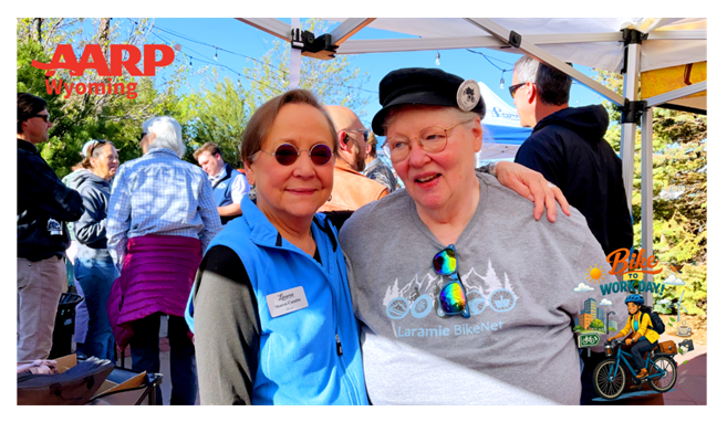 Two women smiling together outdoors under a tent at an event.