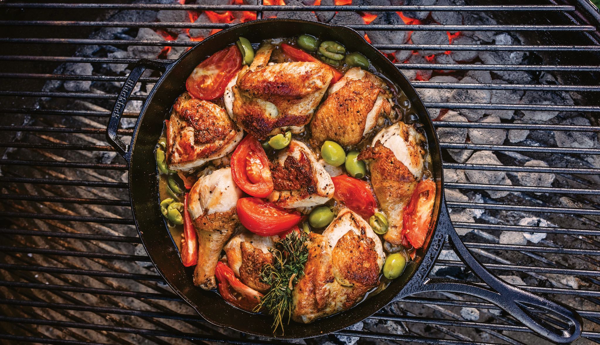 Michael Symon's French-Style Roasted Chicken Recipe roasted chicken in a cast iron pan with olives and tomato