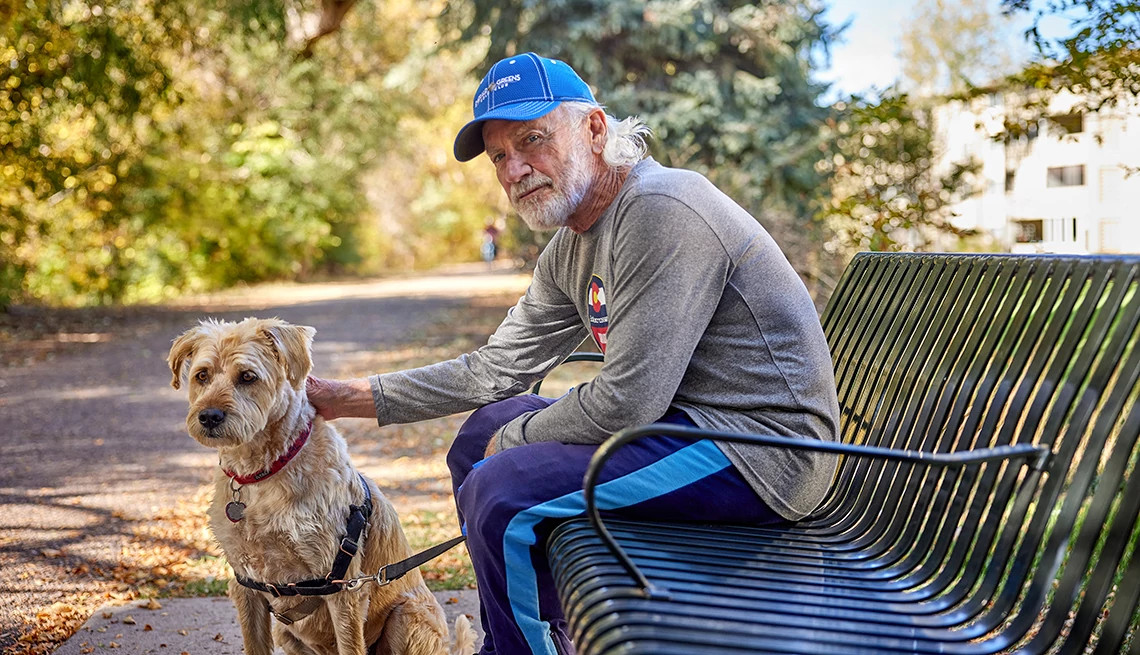 A senior man sits on a park bench with his dog