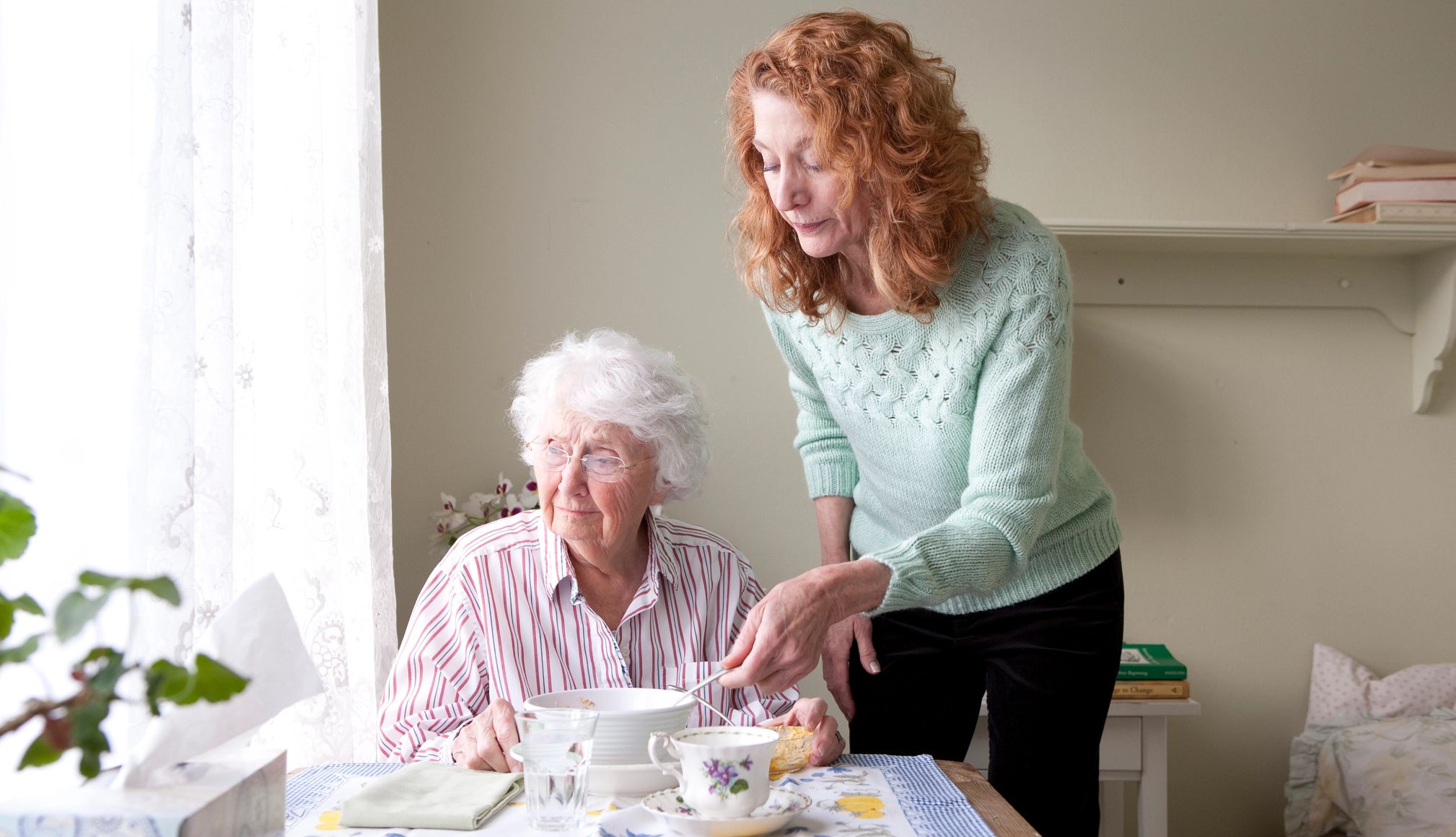 Caregiving bankruptcy a woman cares for an older woman during mealtime