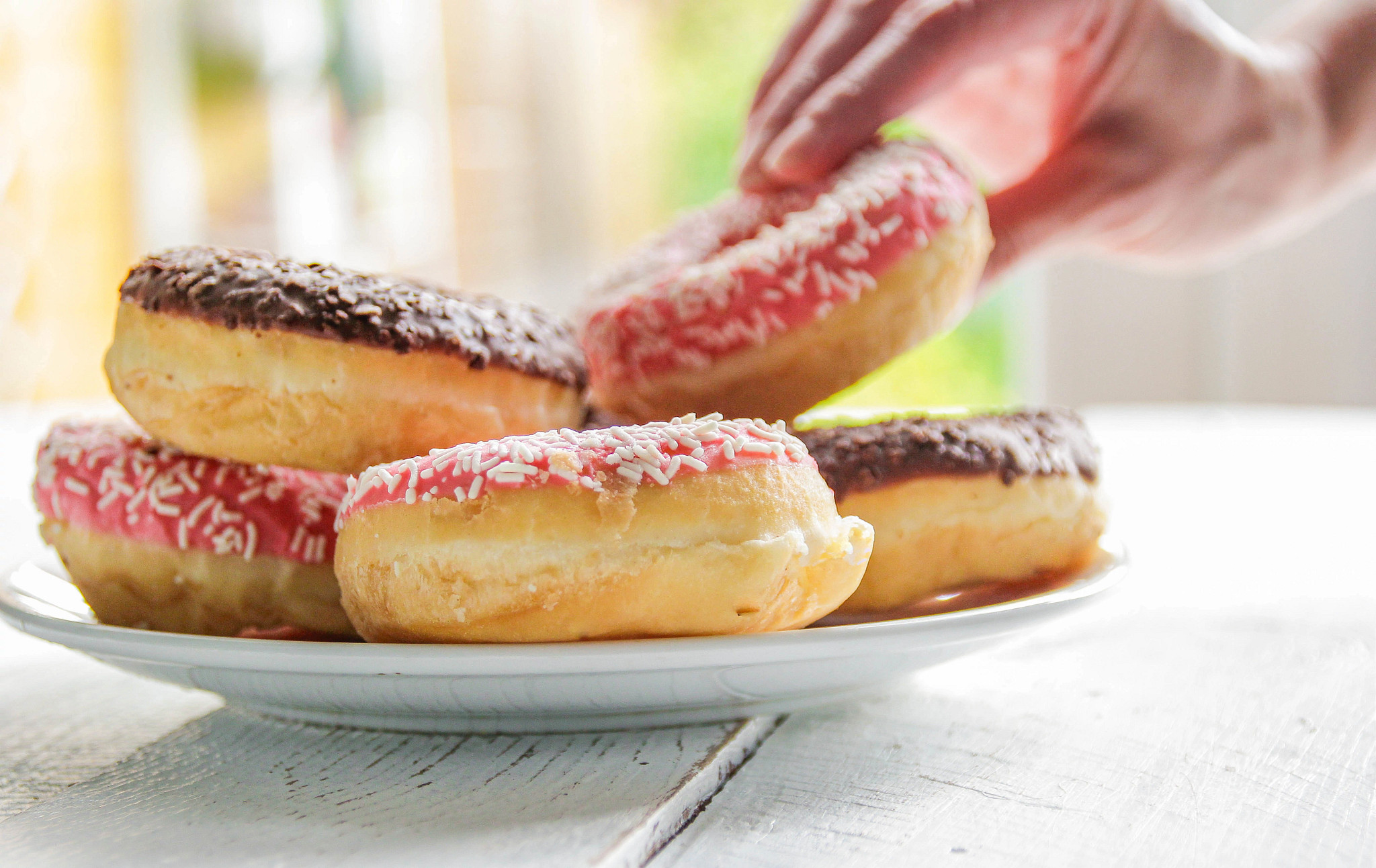 a close up view of a plate of frosted doughnuts, with a person's hand lifting one