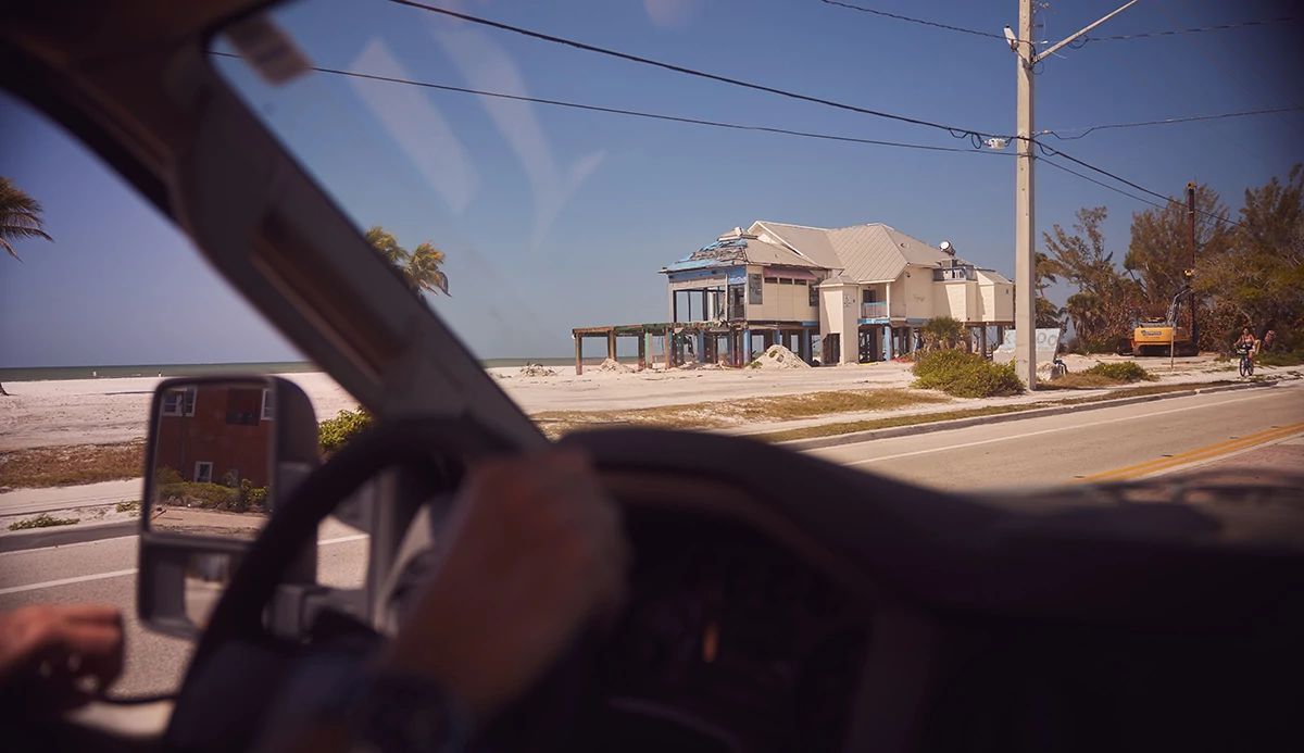 A damaged beach house seen through the windshield of a vehicle
