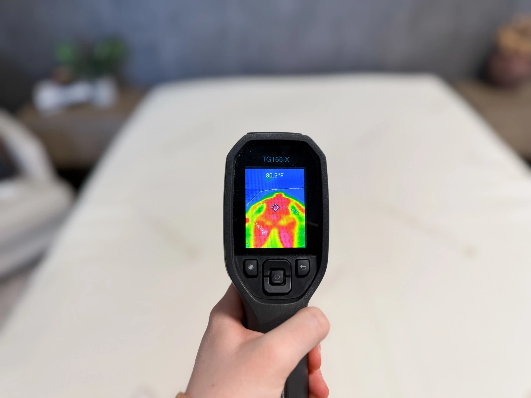 A person points a temperature-reading tool at a mattress 