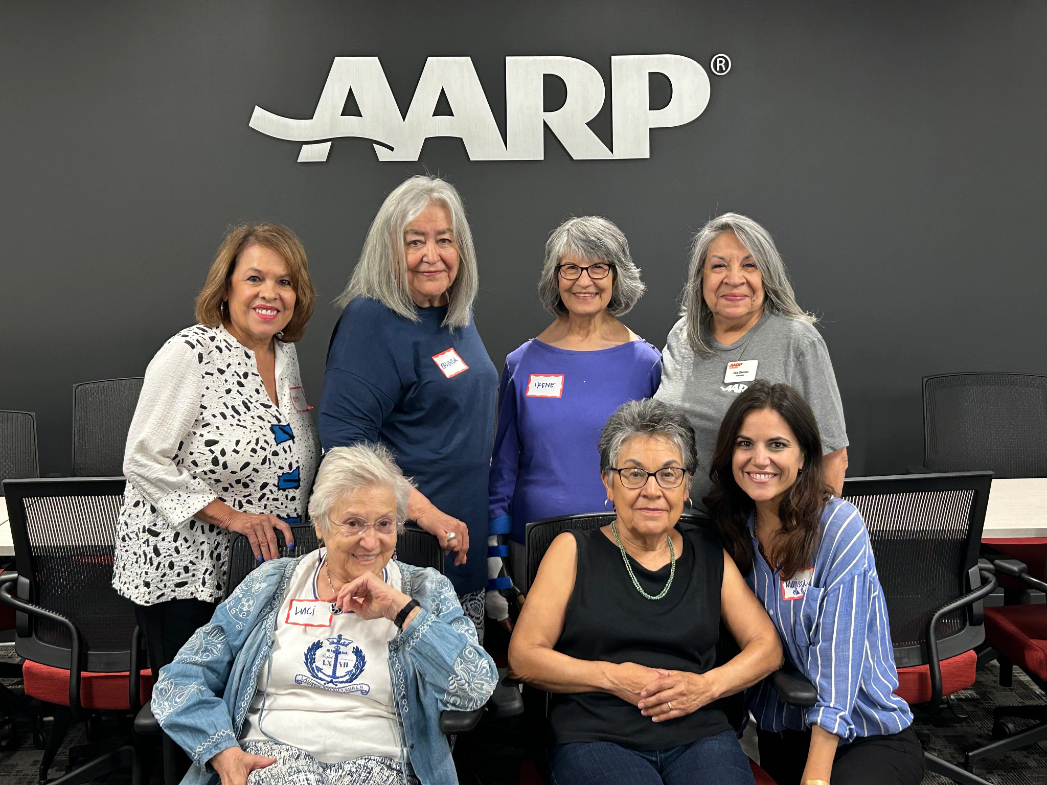 A portrait of seven multi-generational Latina women pose for a photo in the AARP Colorado office