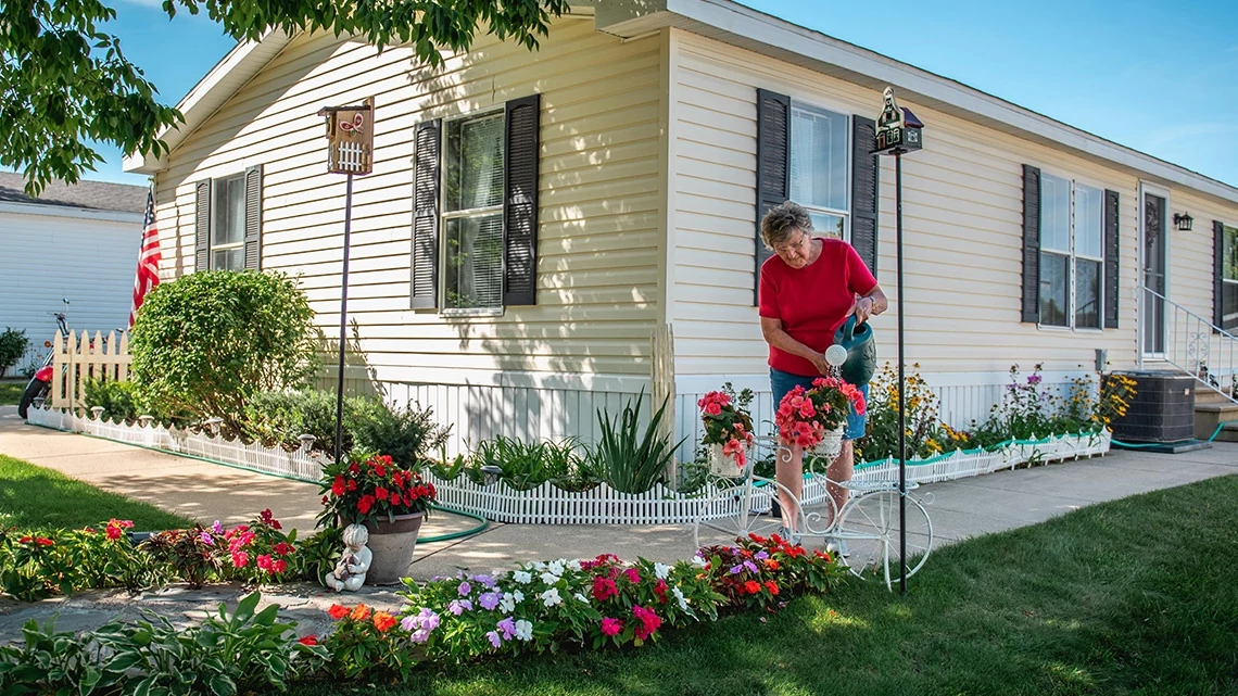 Woman watering flowers mobile home white with black shutters