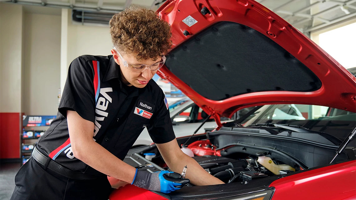 Valvoline Instant Oil Change person working on the engine of a red car