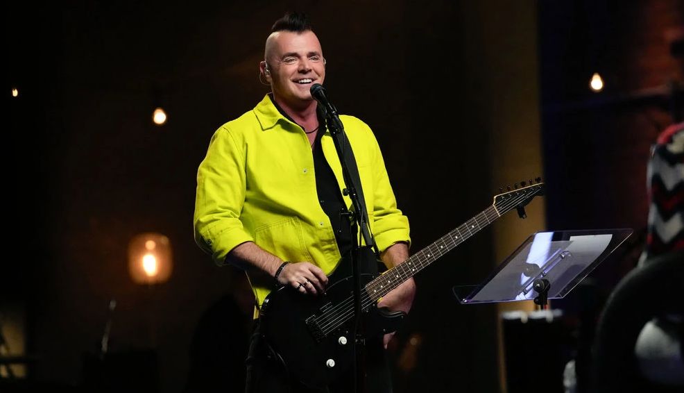 The Voice contestant Bryan Olesen smiling in front of a microphone with his electric guitar during the Pretaped Playoffs