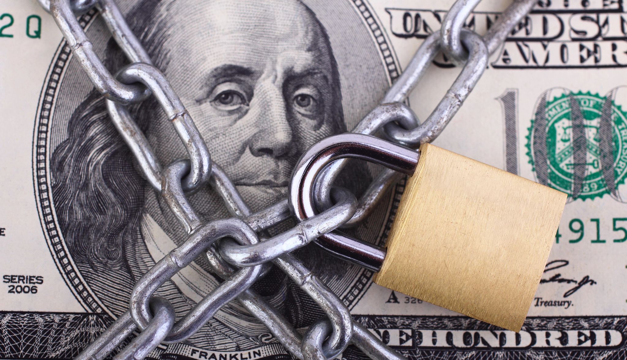 A $100 bill with Ben Franklin's image behind a lock and chains, symbolizing A $100 bill with Ben Franklin's image behind a lock and chains, symbolizing