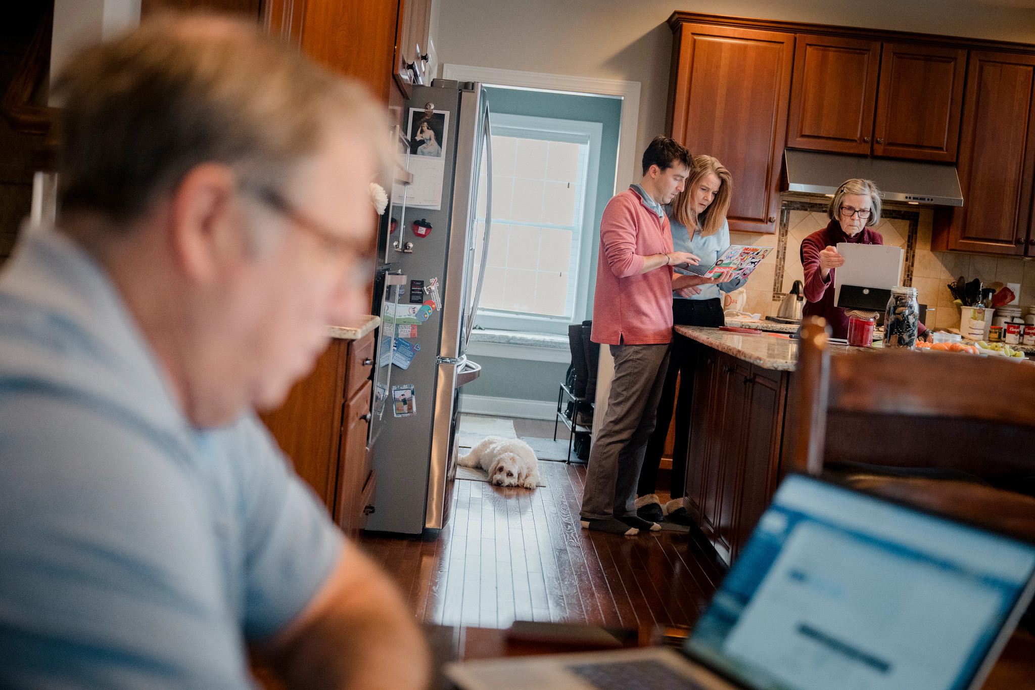 tres adultos revisan una laptop y papeles; un hombre mayor usa otra en primer plano.