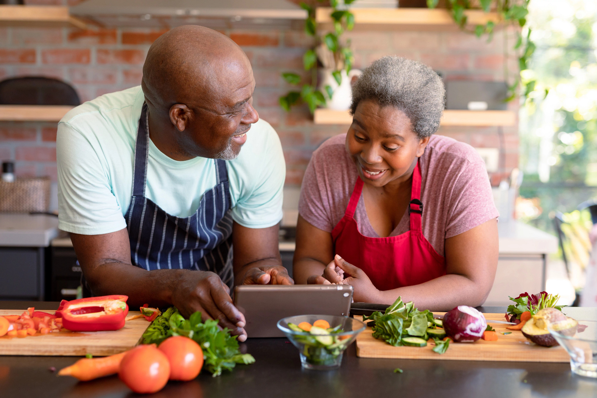 Un hombre y una mujer en la cocina miran una receta en una pantalla con alimentos a su alrededor.
