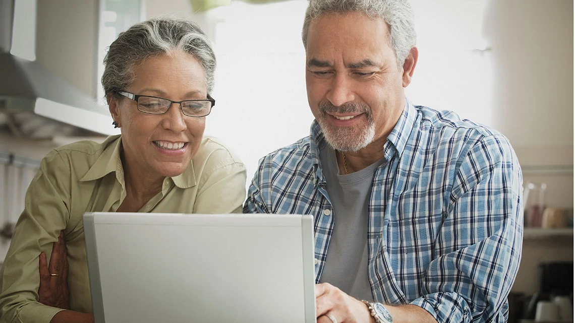 AARP® Medicare Plans from UnitedHealthcare Smiling, mature Hispanic man, woman looking at laptop in kitchen