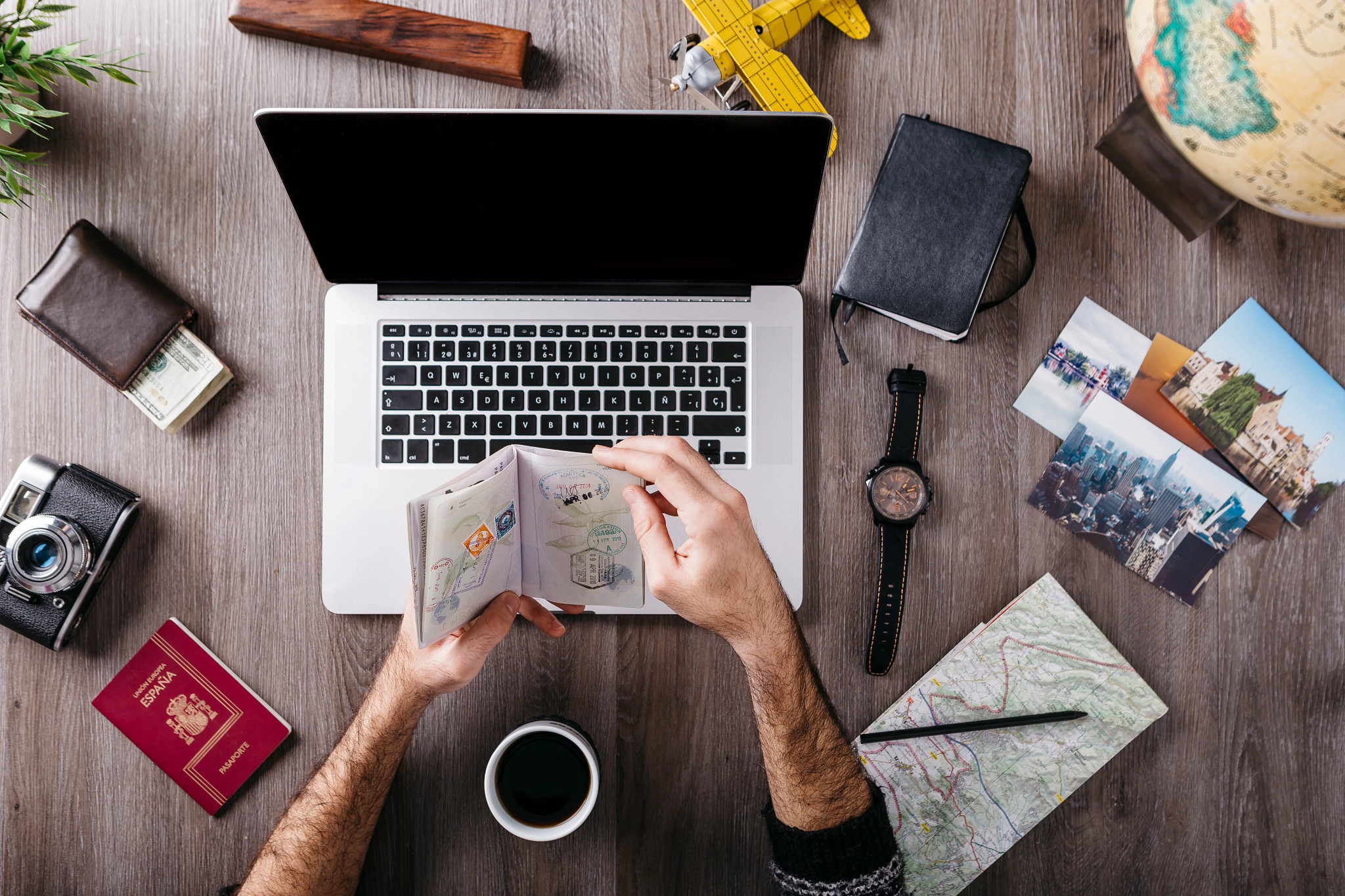 an aerial photo of hands flipping through a passport in front of a laptop