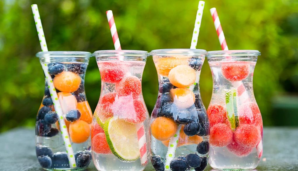 Staying hydrated with water rather than soda is an important part of everyday health Four carafes of fruit-infused water on a table outside