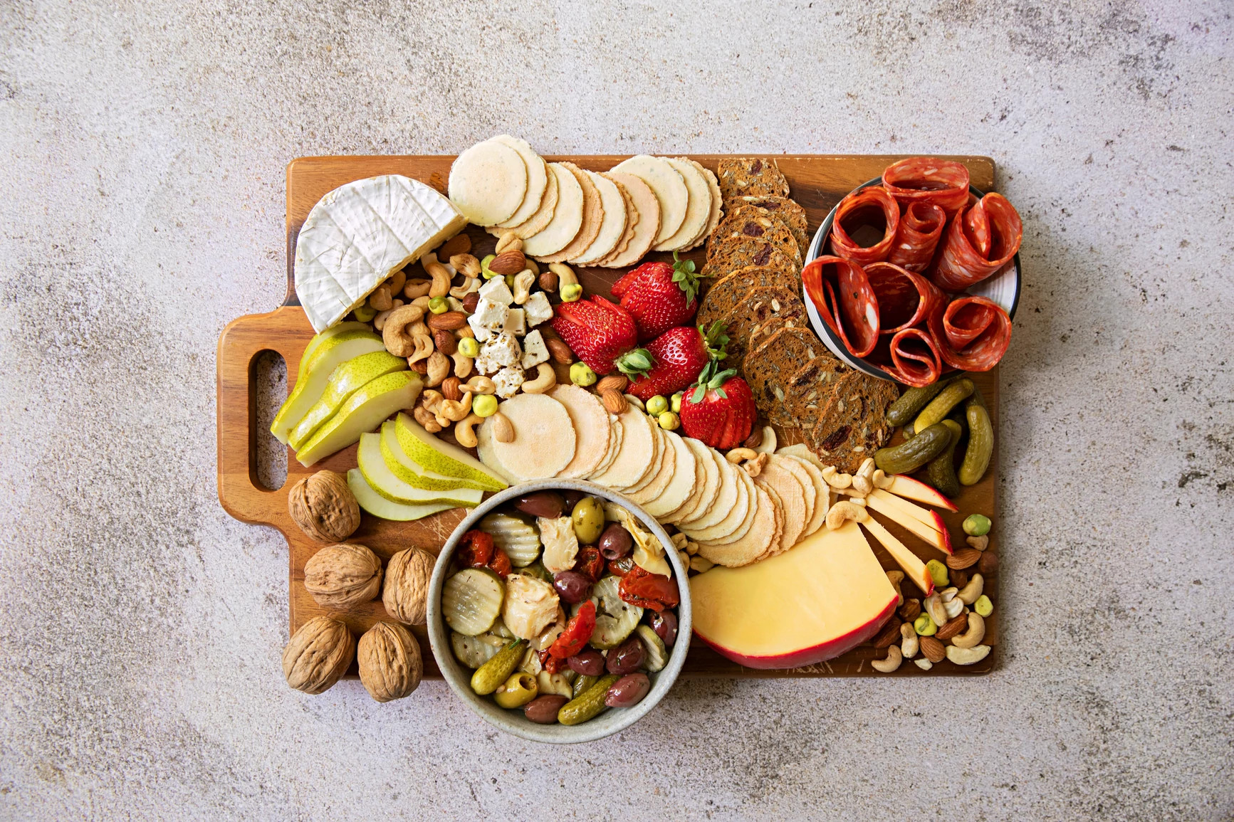 charcuterie board with fruit, cheese, pickles, meat, bread and nuts