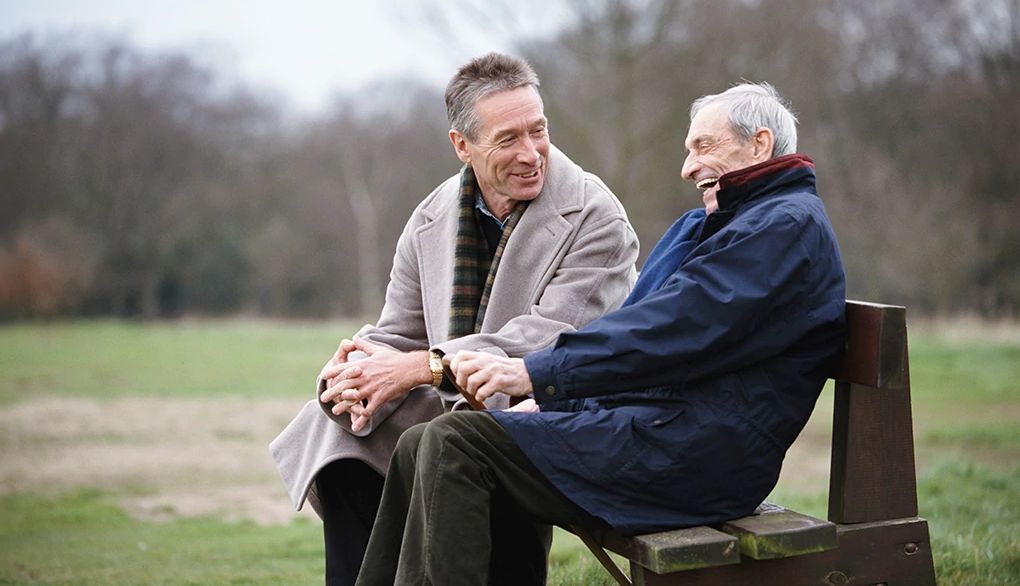 The company you keep can affect your mood Two men smiling and talking to each other on a park bench