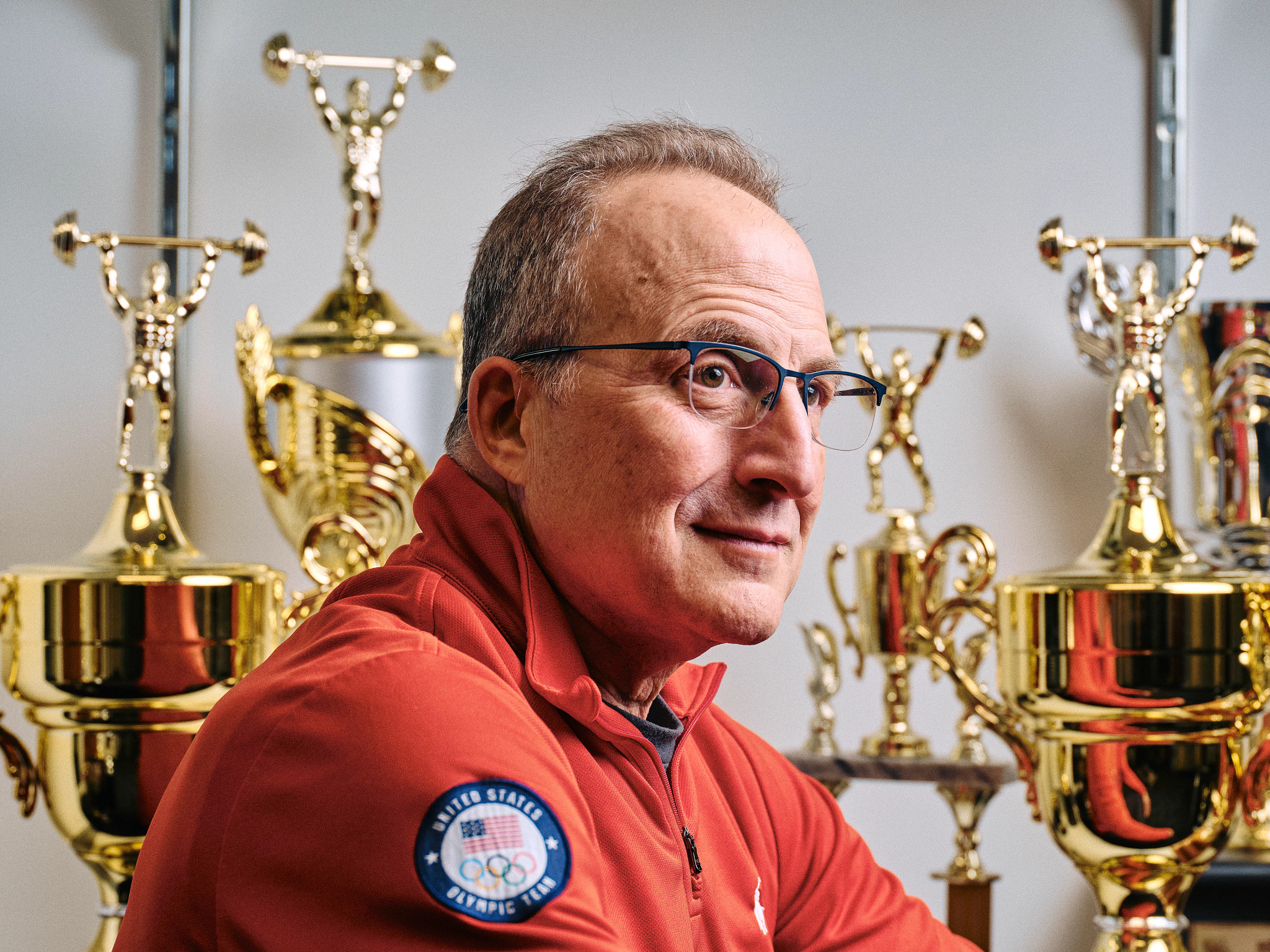 Senior Director of Sport Performance & Coaching Education for USA Weightlifting Team Mike Gattone with trophies behind him.