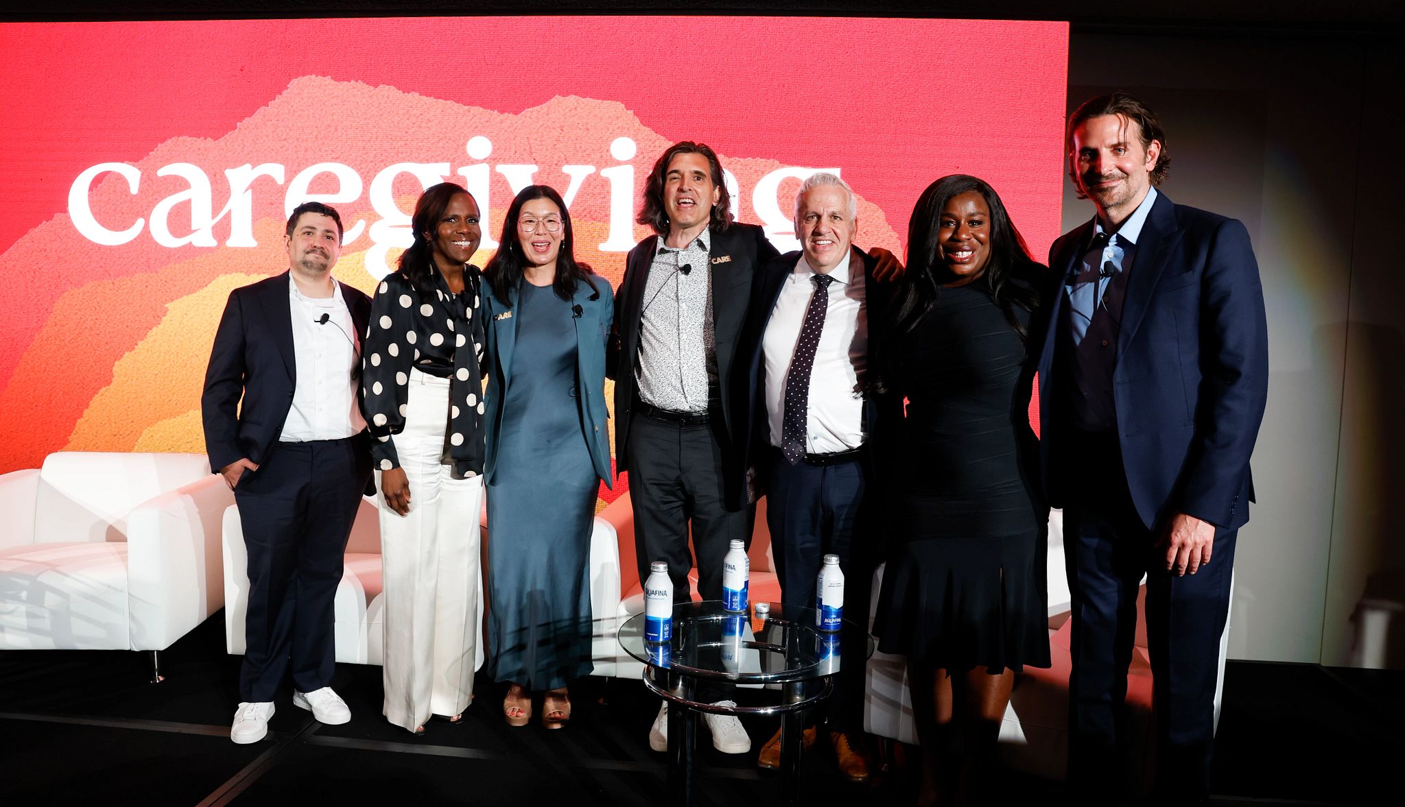 Bradley Cooper Caregiving Documentary a group of people smile for the camera in front of a backdrop that says caregiving
