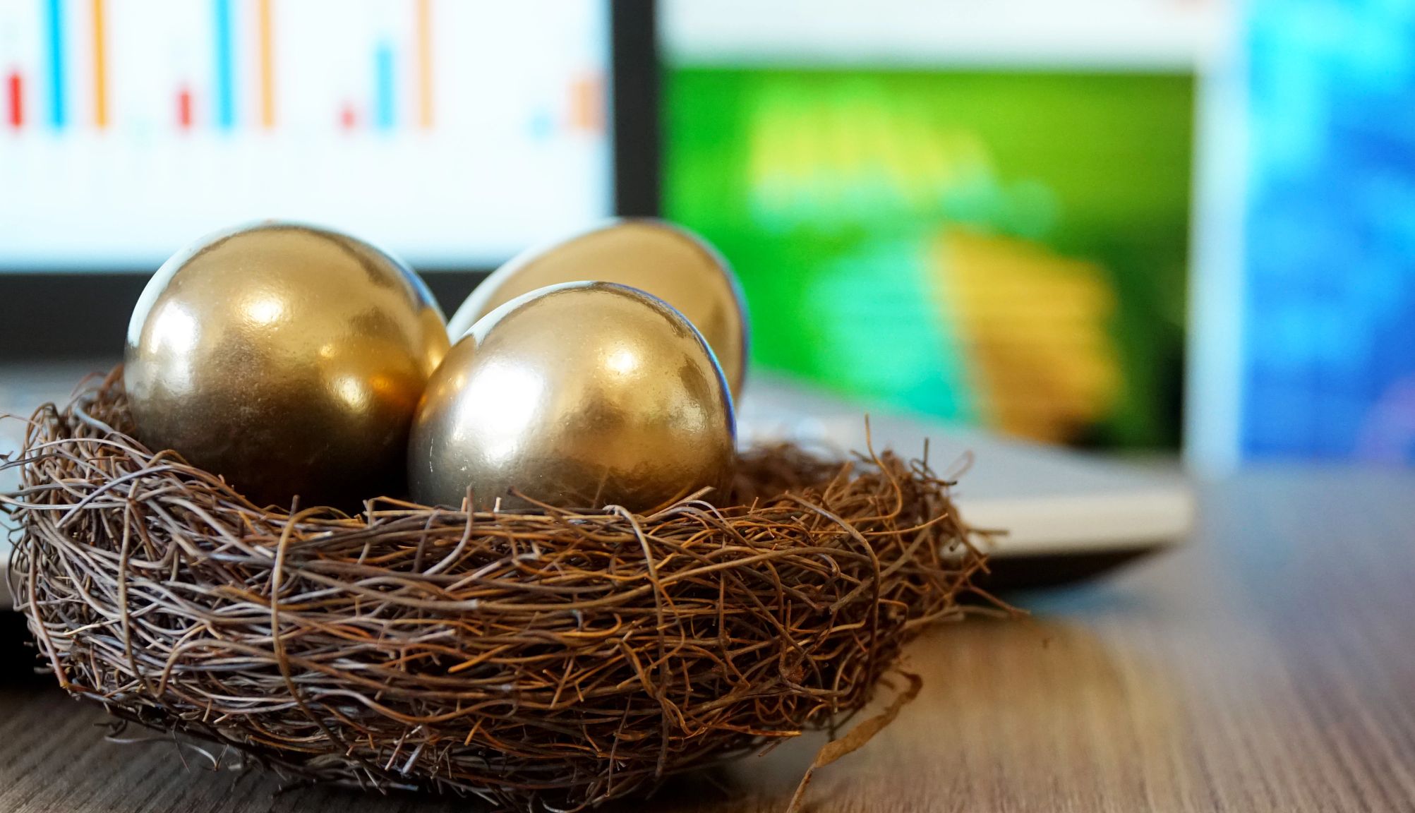 Un nido con tres huevos dorados encima y una computadora portátil en el fondo