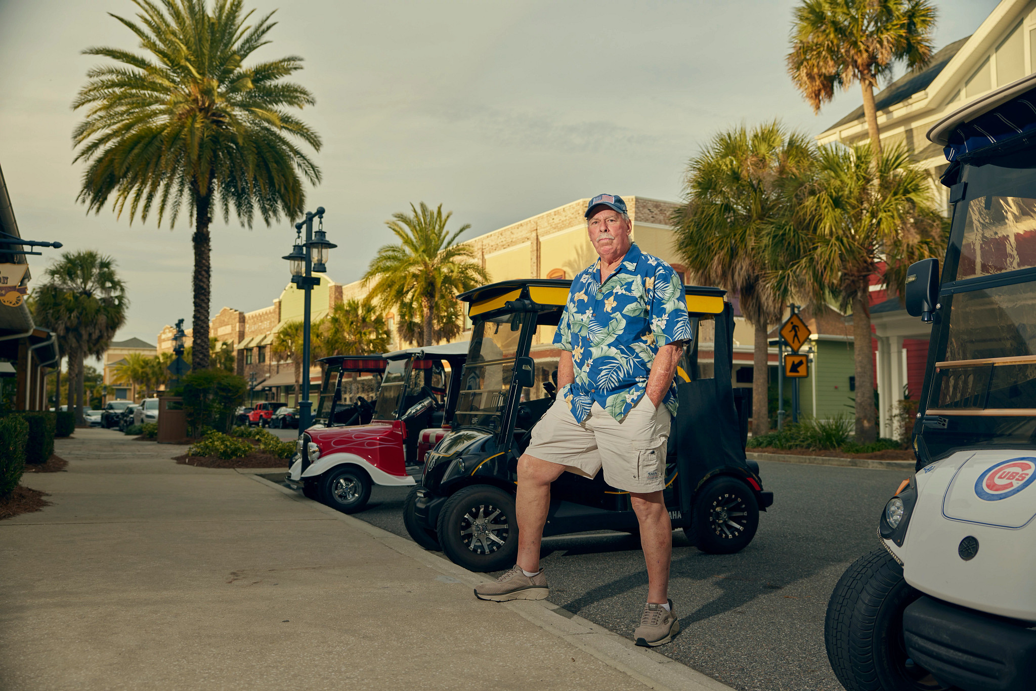 a man in a floral print shirt stands in front of golf carts