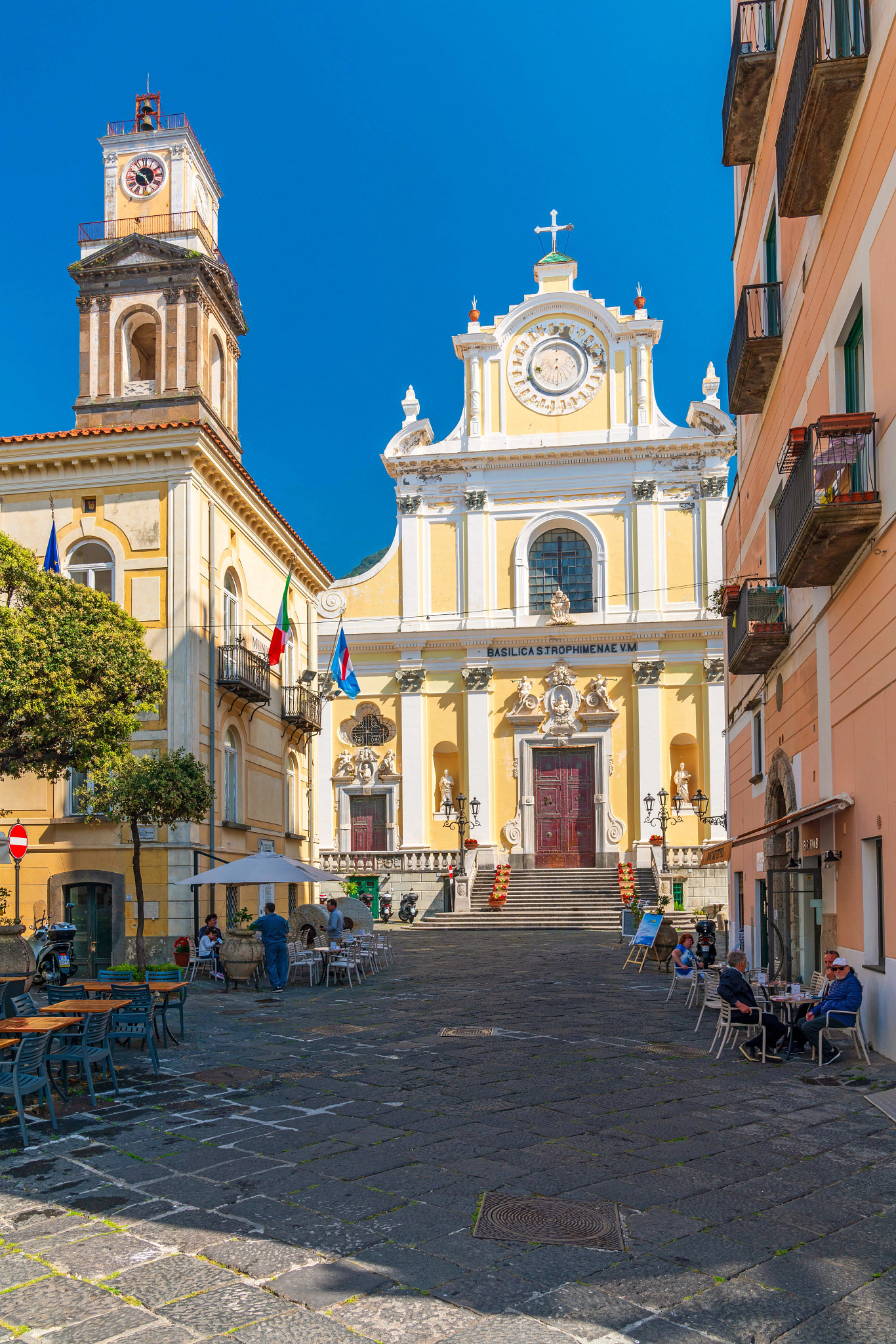 Historic cathedral and clock tower in Italy overlooking a charming piazza with outdoor cafés.