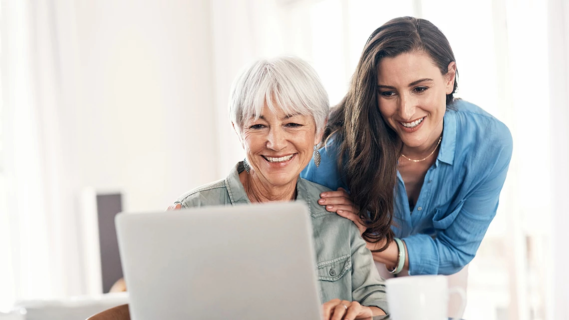 Savi Student Loan Repayment Tool woman with white short hair looking at laptop while woman with long brown hair stands over her shoulders looking at what is on screen