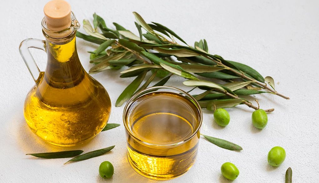 Extra-virgin olive oil contains heart-healthy monounsaturated fatty acids An up-close view of olive oil and olives on a white background