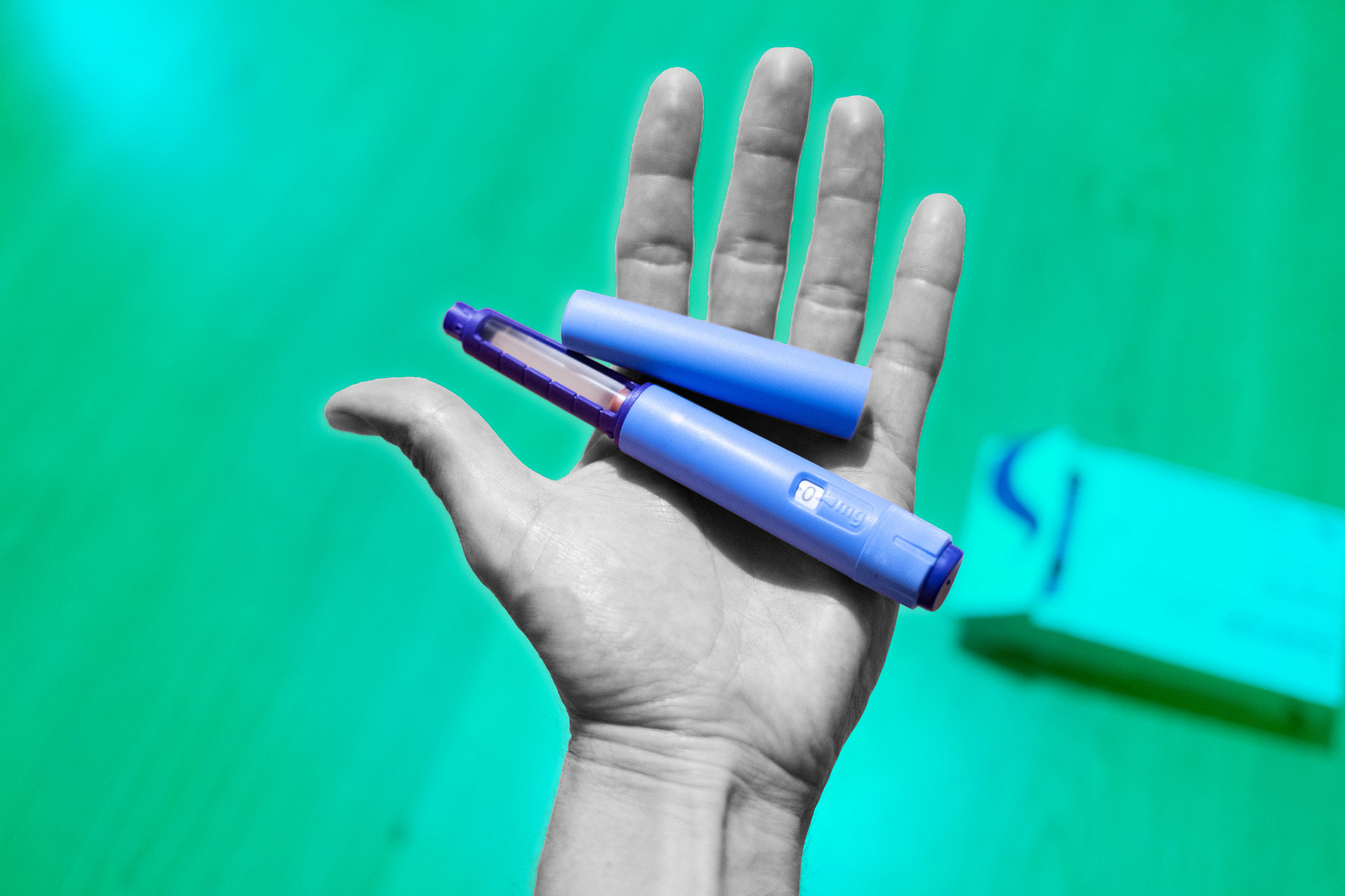 An open hand holding a blue GLP-1 weight loss injection pen next to its cap.