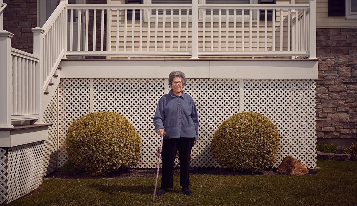 a lady standing in front of a house with a raised front porch