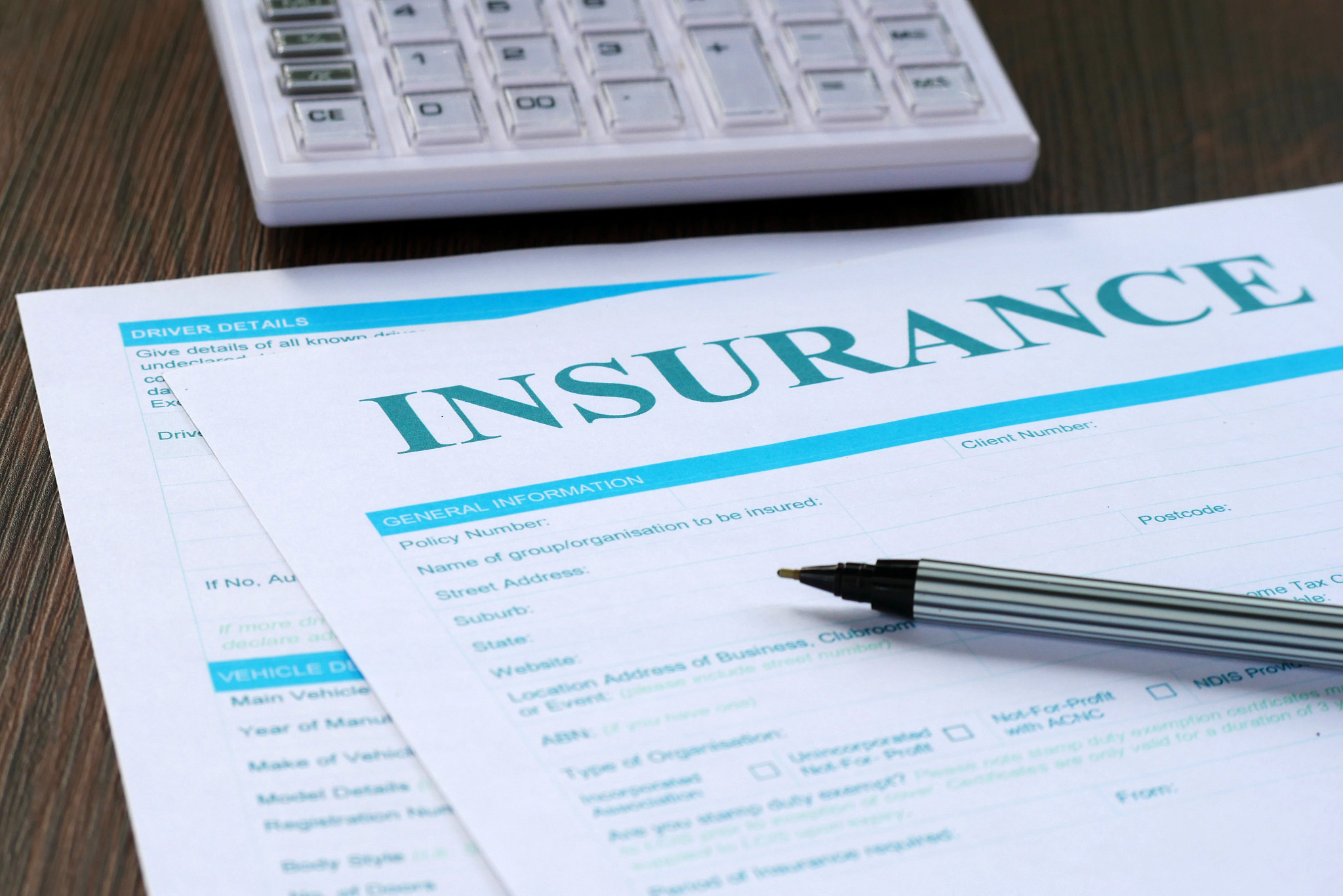 A writing pen sits on top of an insurance form with a calculator within reach.