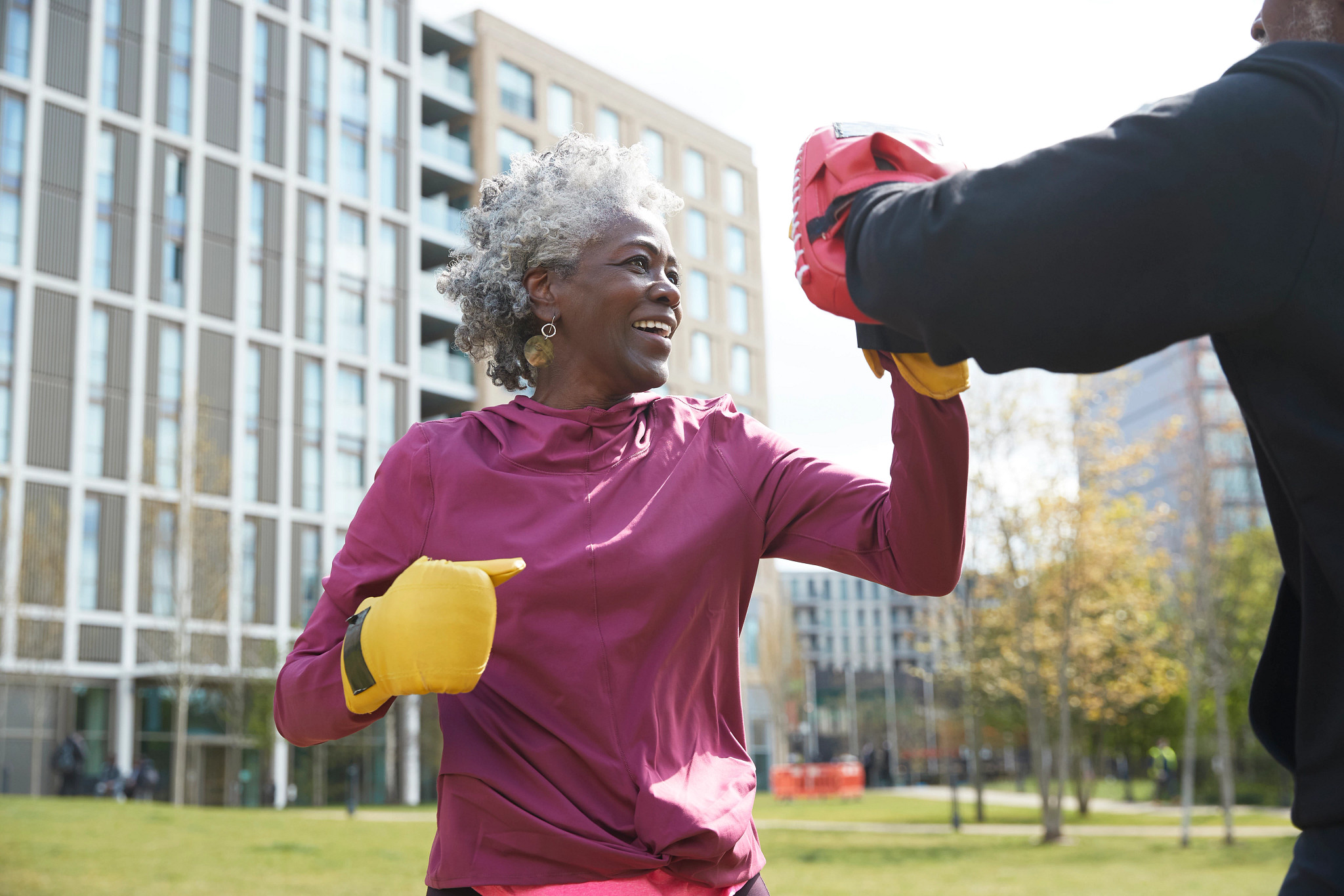 A woman practices boxing in a park on a sunny day.