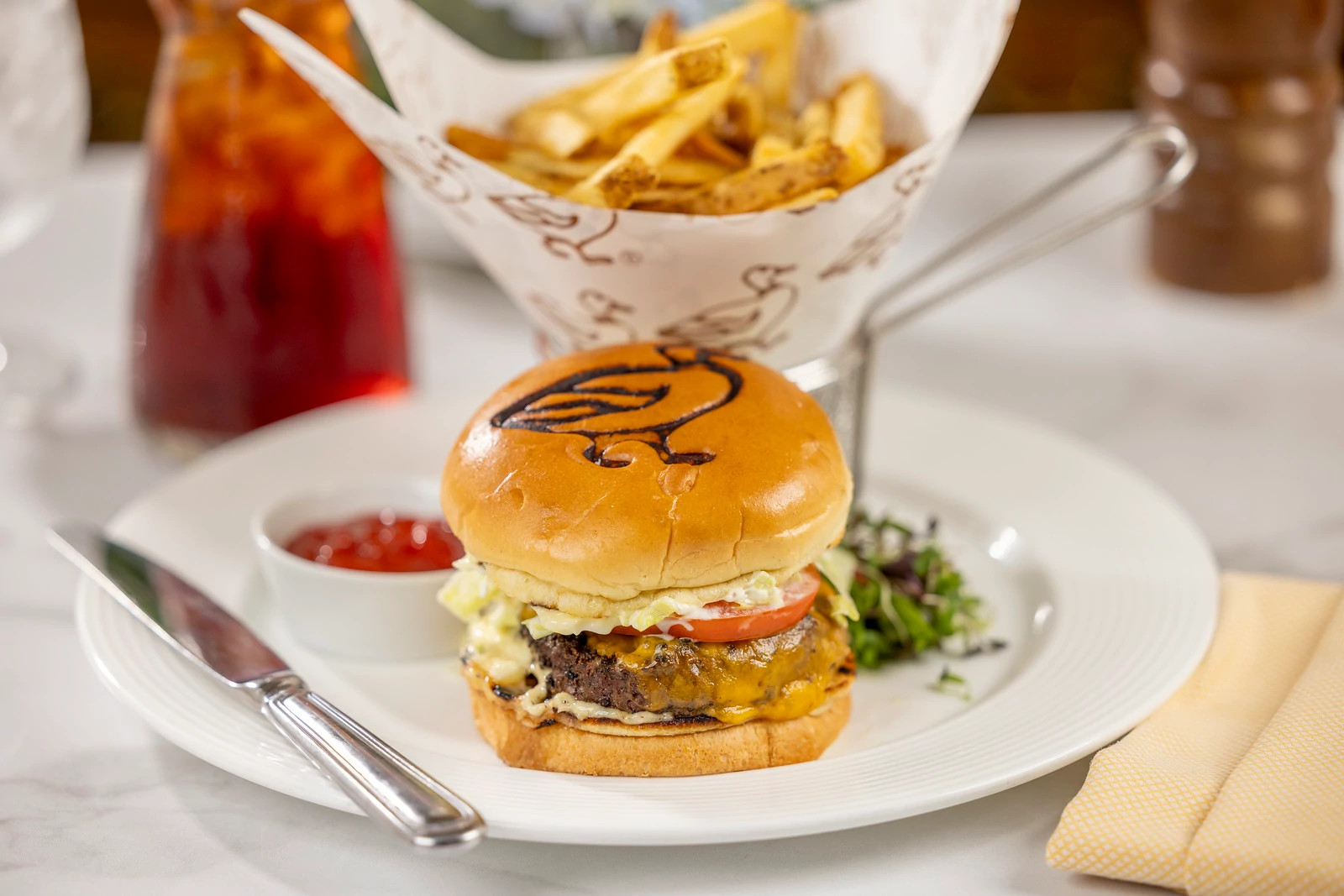 Restaurant lunch featuring a gourmet cheeseburger, crispy fries, salad greens, and a beverage.
