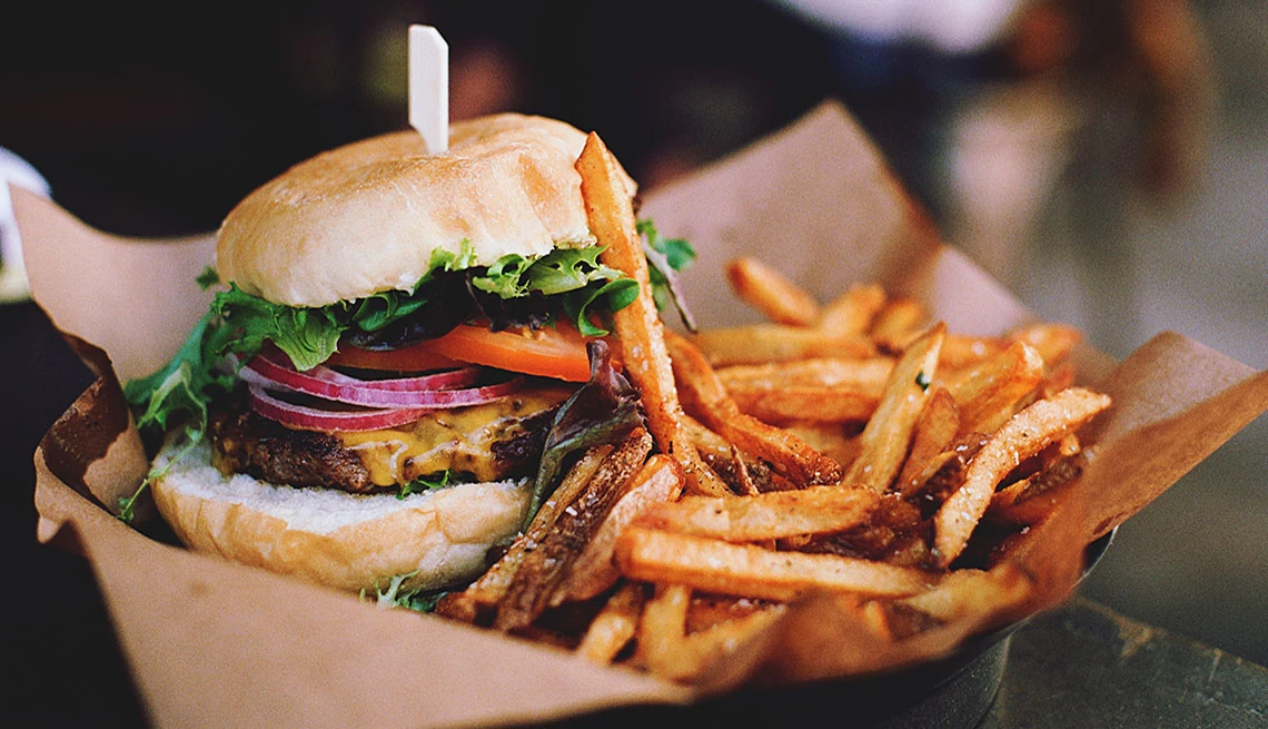 Restaurant Savings Near You cheeseburger lettuce tomato red onion sweet potato fries on brown paper black container