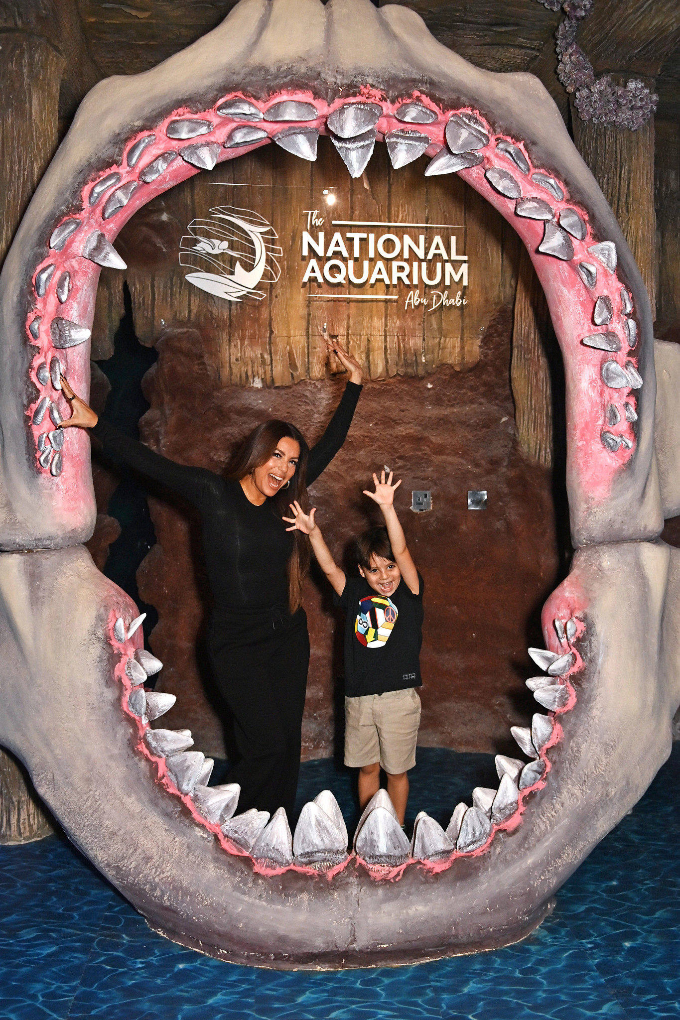 eva longoria and her son posing inside a large replica of a sharks jaw