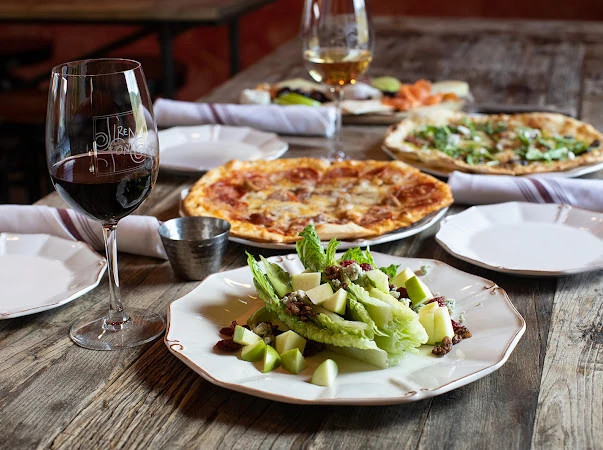 Several plates of food and glass of red wine on table