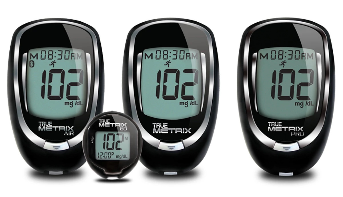 A professional product shot features four black and silver digital blood glucose monitors from the TRUE METRIX brand, all displaying a reading of 102 mg/dL.