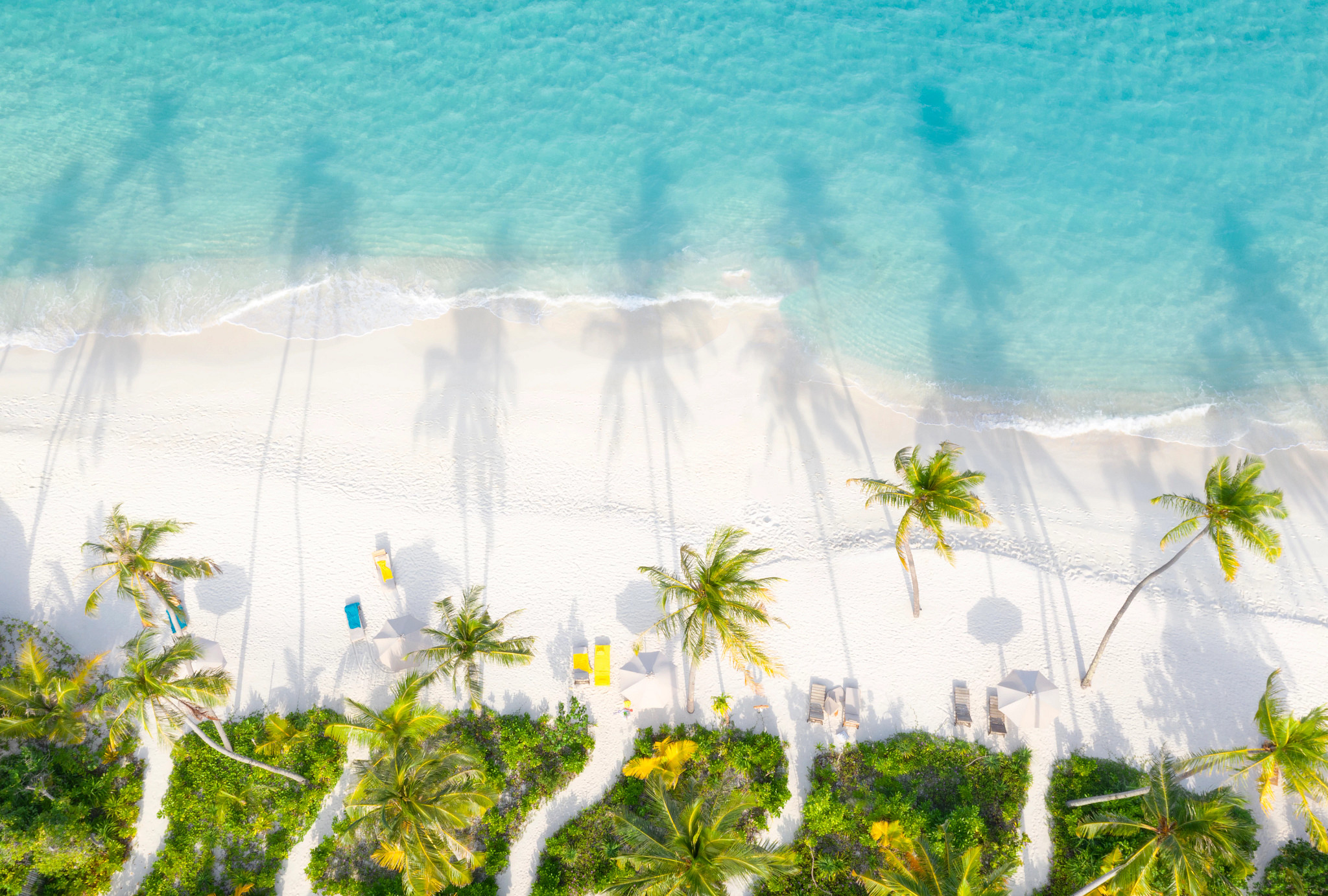 Aerial of the beautiful secluded white sand beach on a small Maldives island. Sun setting casting shadows in to the turquoise ocean.