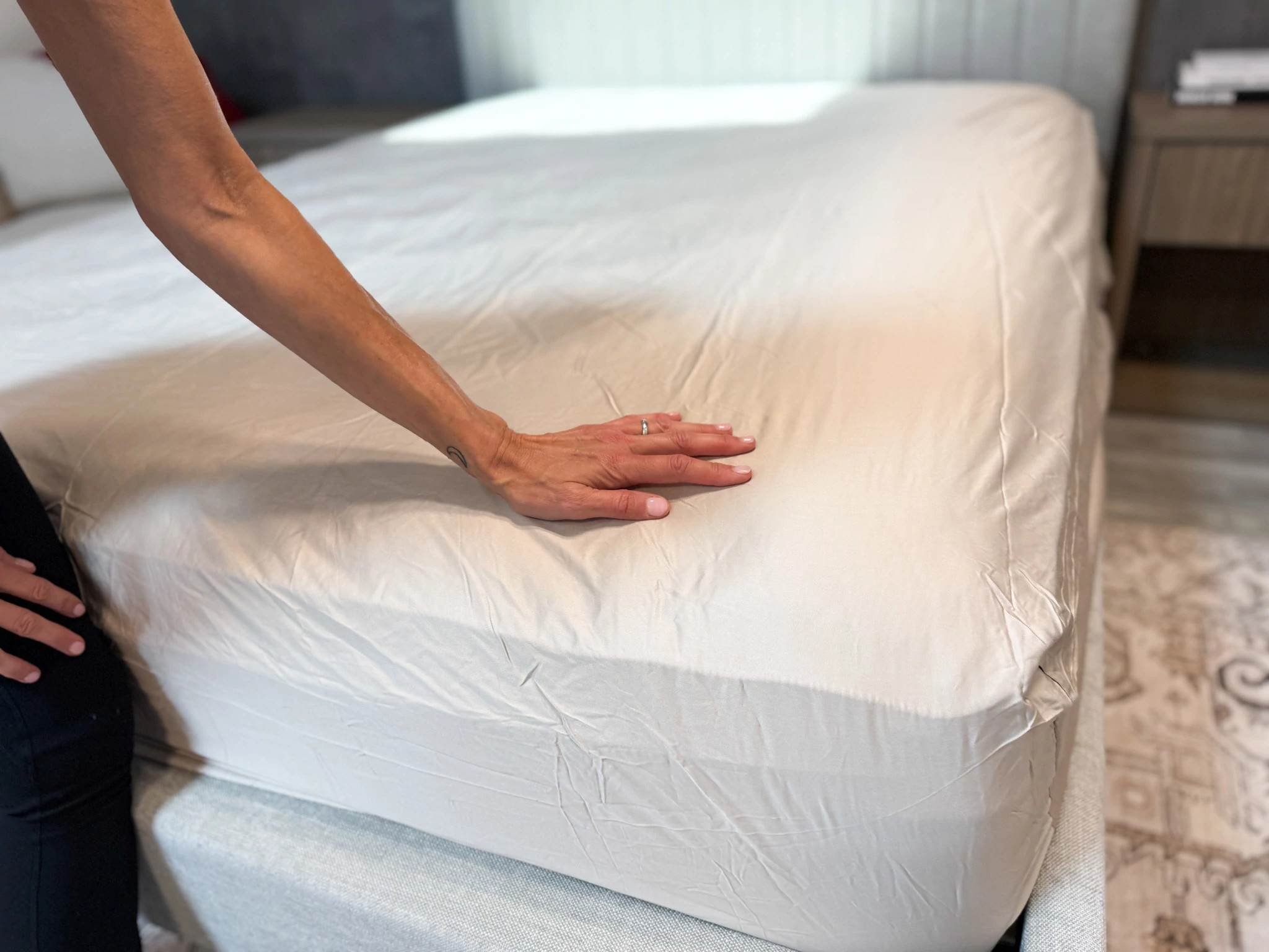 A woman’s hand touching the Quince Bamboo Sheet on a mattress.