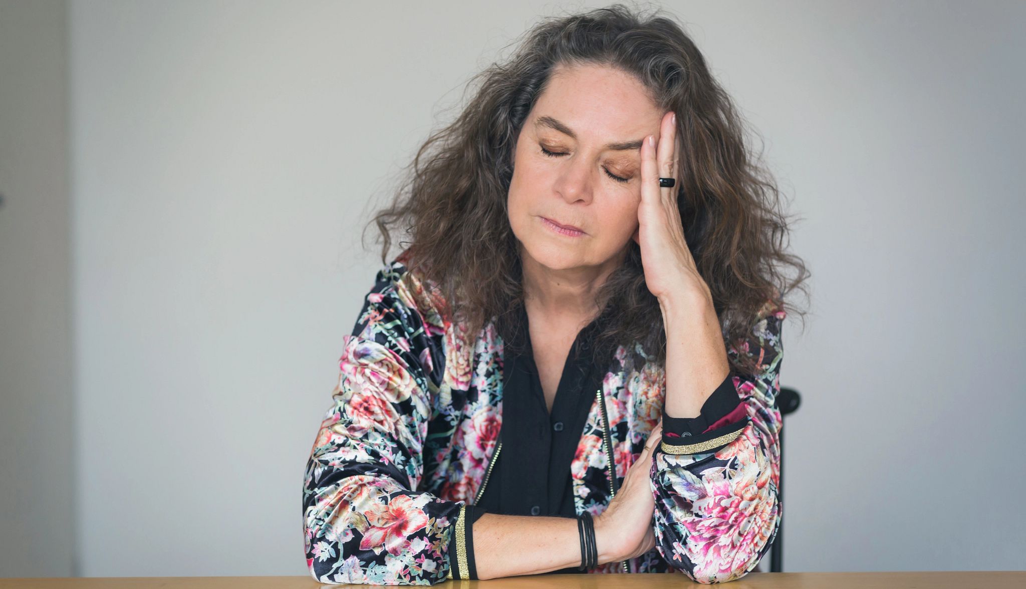 Menopause may affect your mood A woman at a table resting her head on her hand with closed eyes and a withdrawn expression