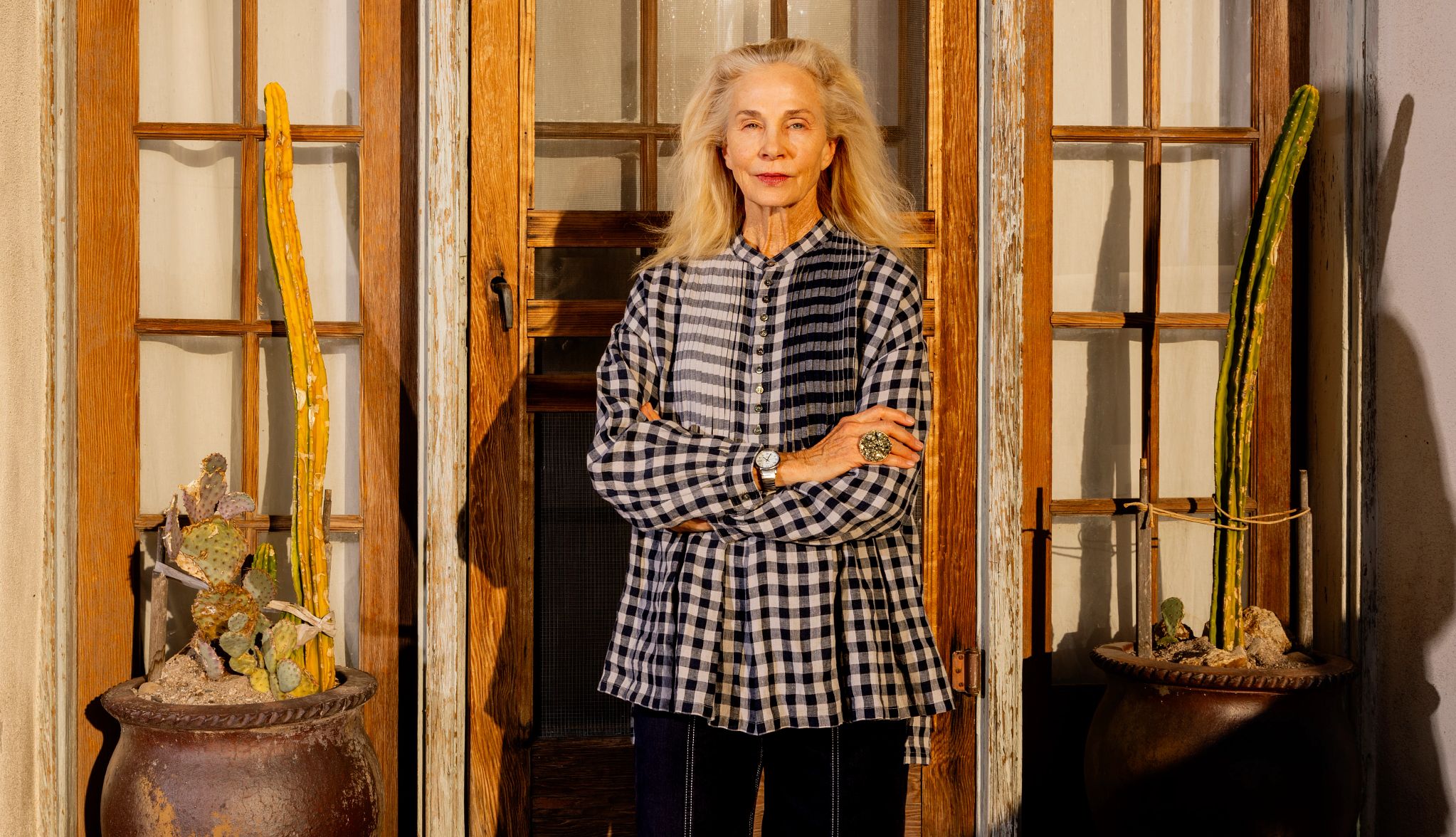 Kitty Brophy a woman stands, arms crossed, in front of a wooden door and shutters