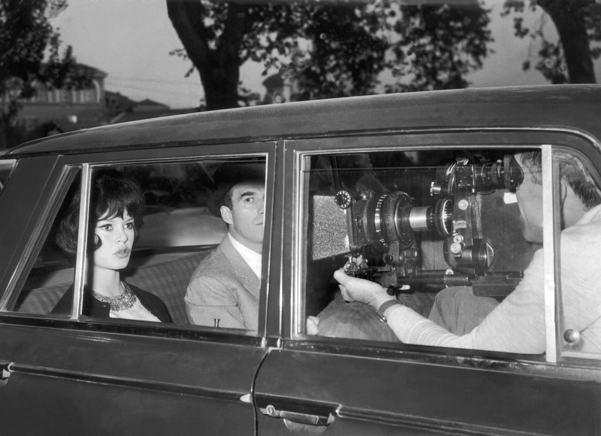 brigitte bardot and a male actor shooting a scene inside a car with a cameraman holding a large cinematic camera