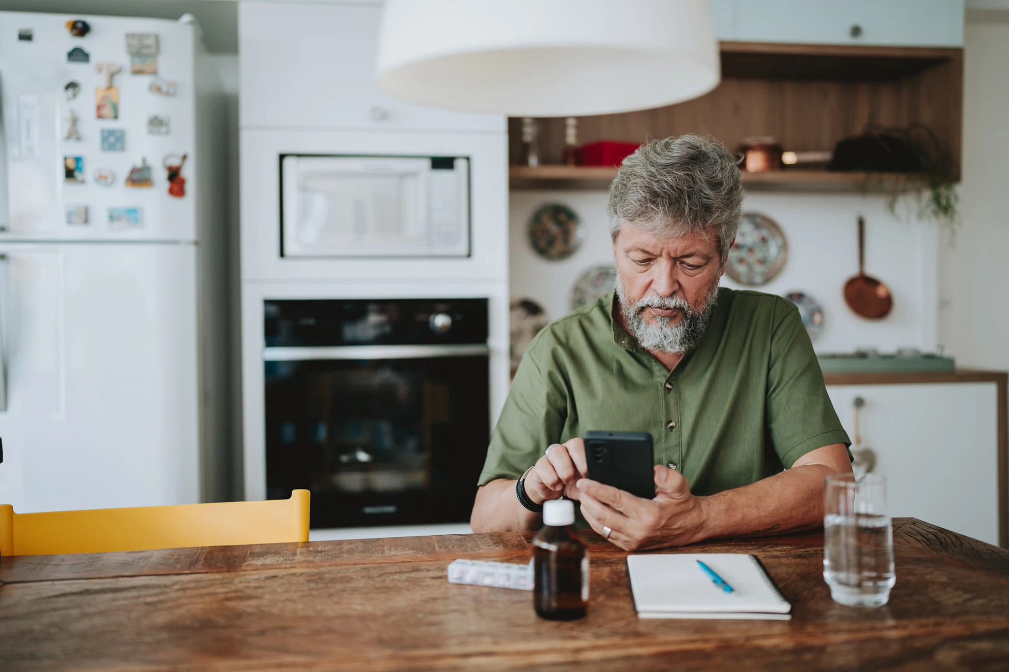 Man looking at smart phone with water and medication Infront of him.