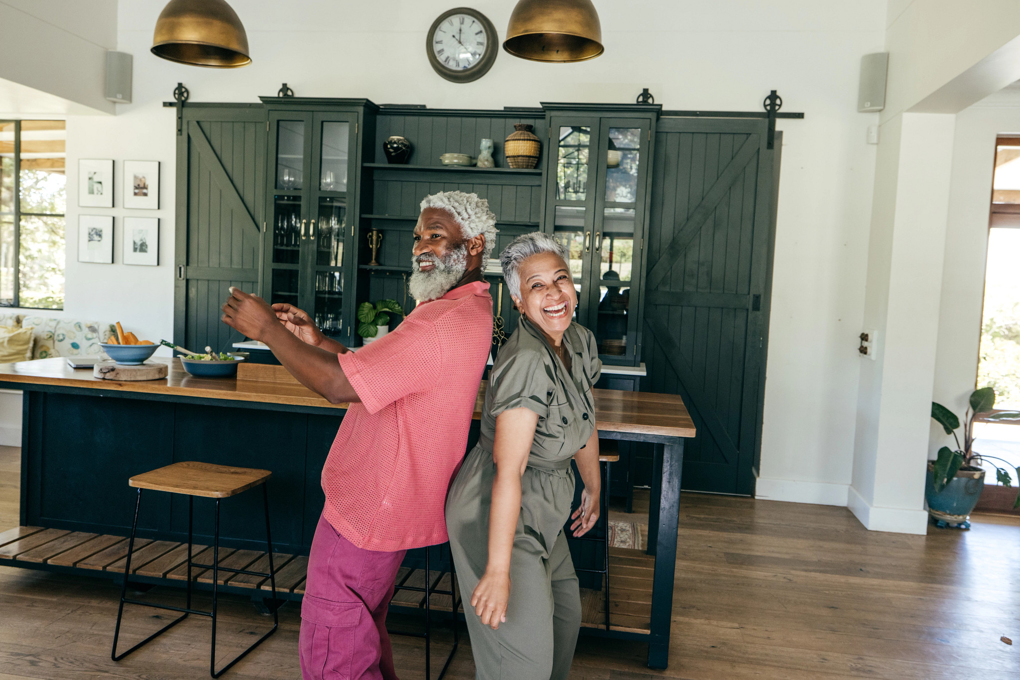 A photo shows an older adult couple playfully dancing in their kitchen