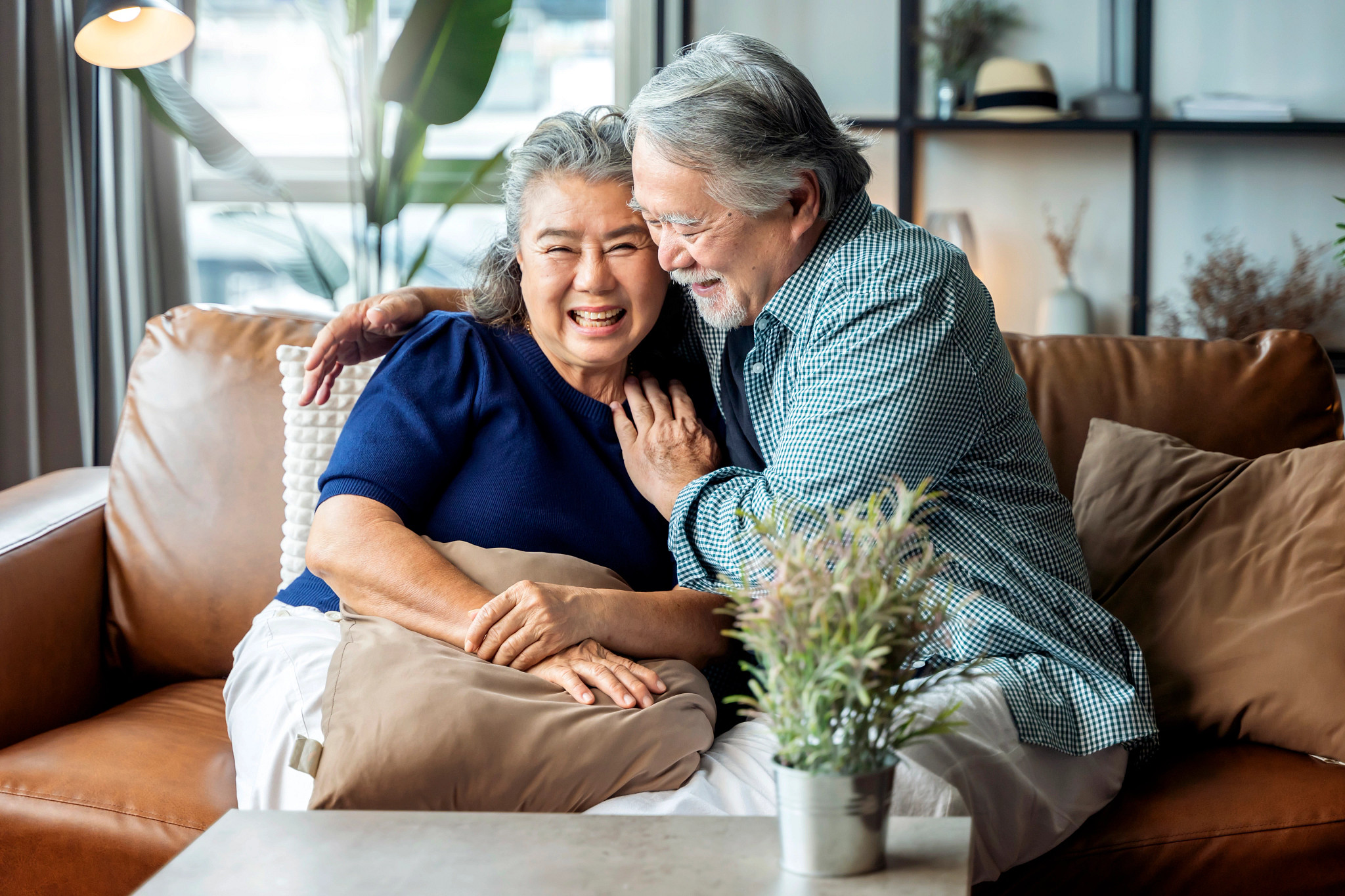 Older Asian couple having a good time laughing while sitting on a couch.