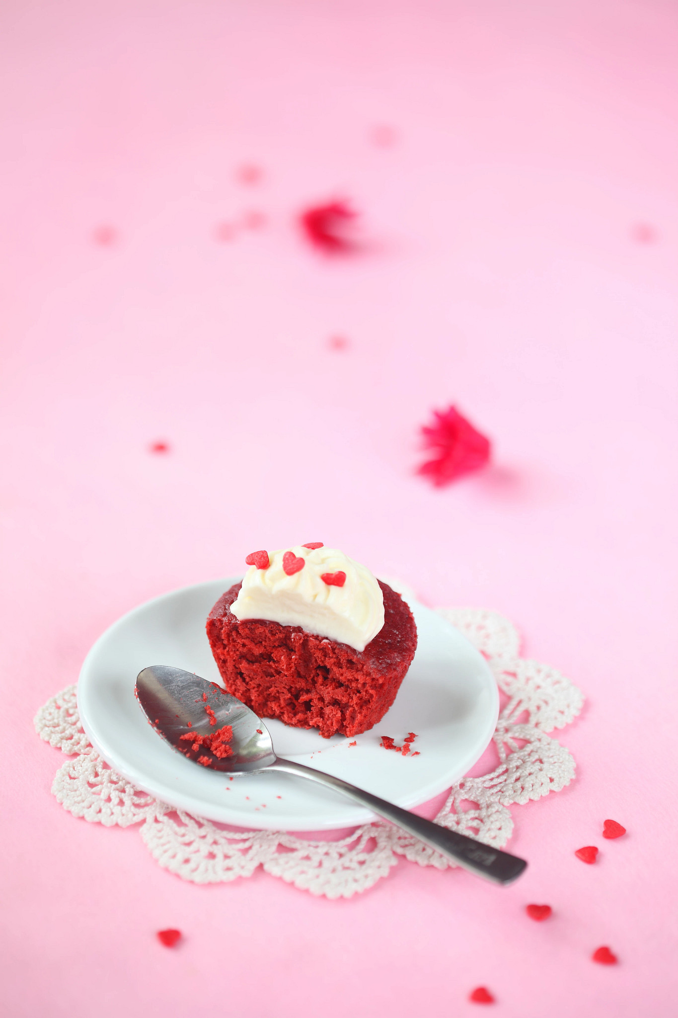 a photo shows a half-eaten Valentine’s Day cupcake on a plate atop a pink table cloth. A spoon is on the plate next to the cupcake
