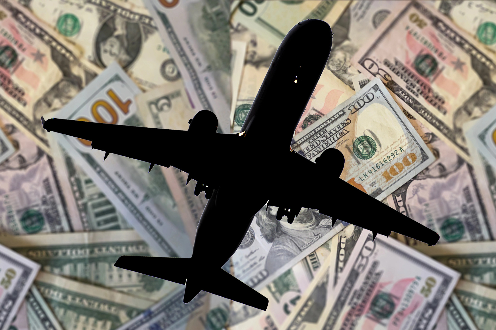 the silhouette of an airplane with dollar bills in the background