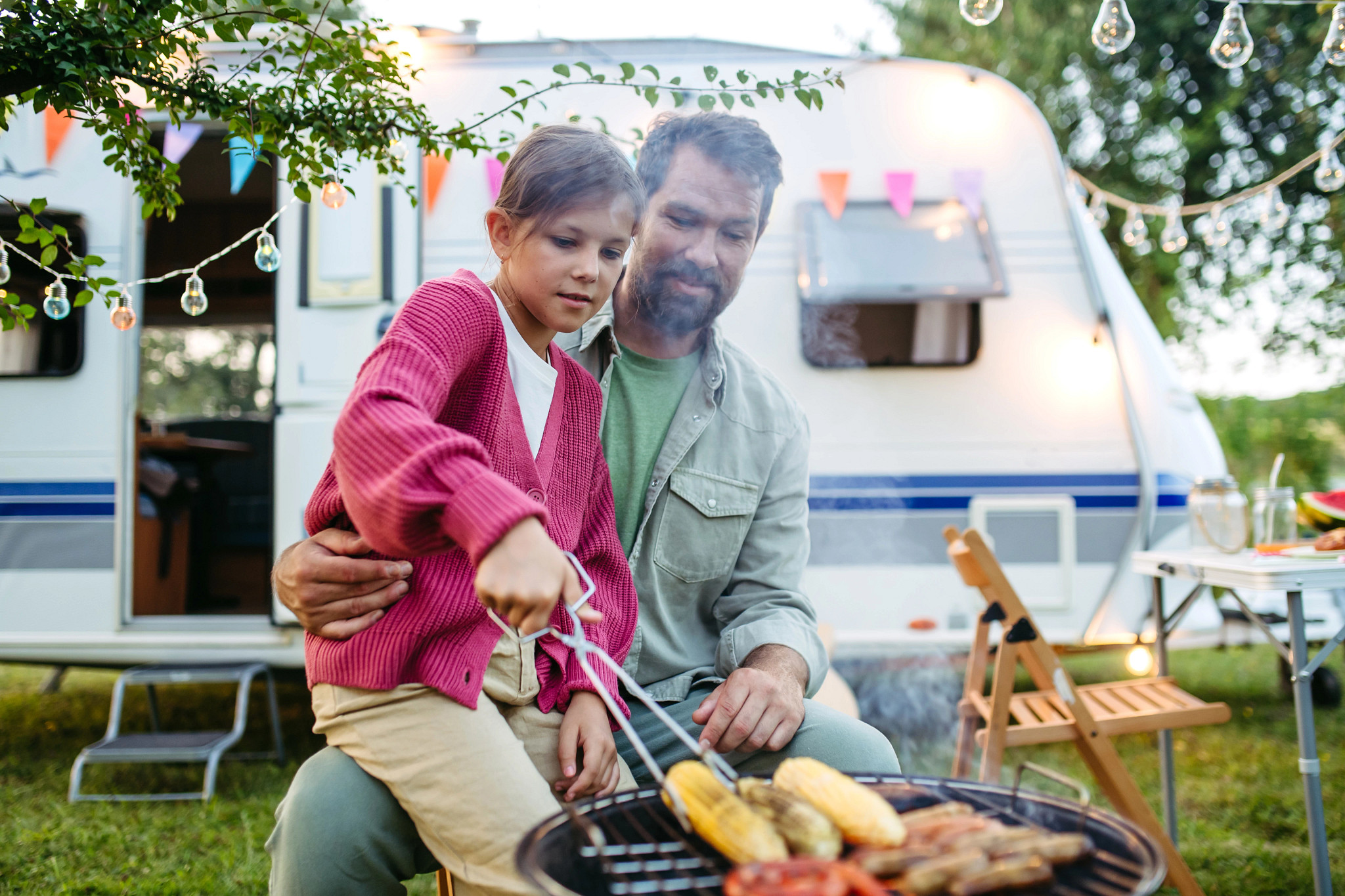 a man with his daughter grilling sausages and corn on the cob