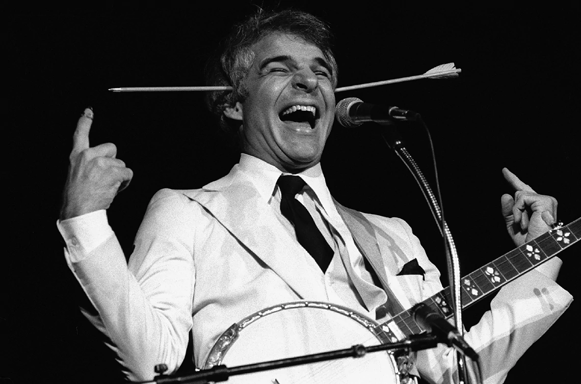 Steve Martin with his banjo while wearing his arrow through the head toy onstage in Chicago